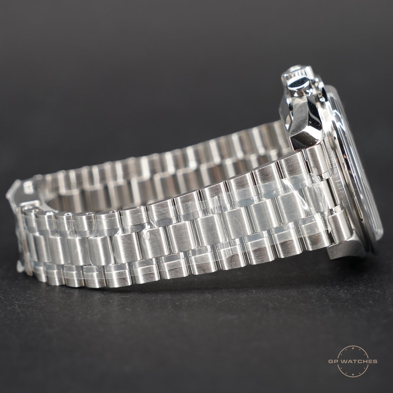 Side view of a silver metal wristwatch with a metal link band against a dark background.