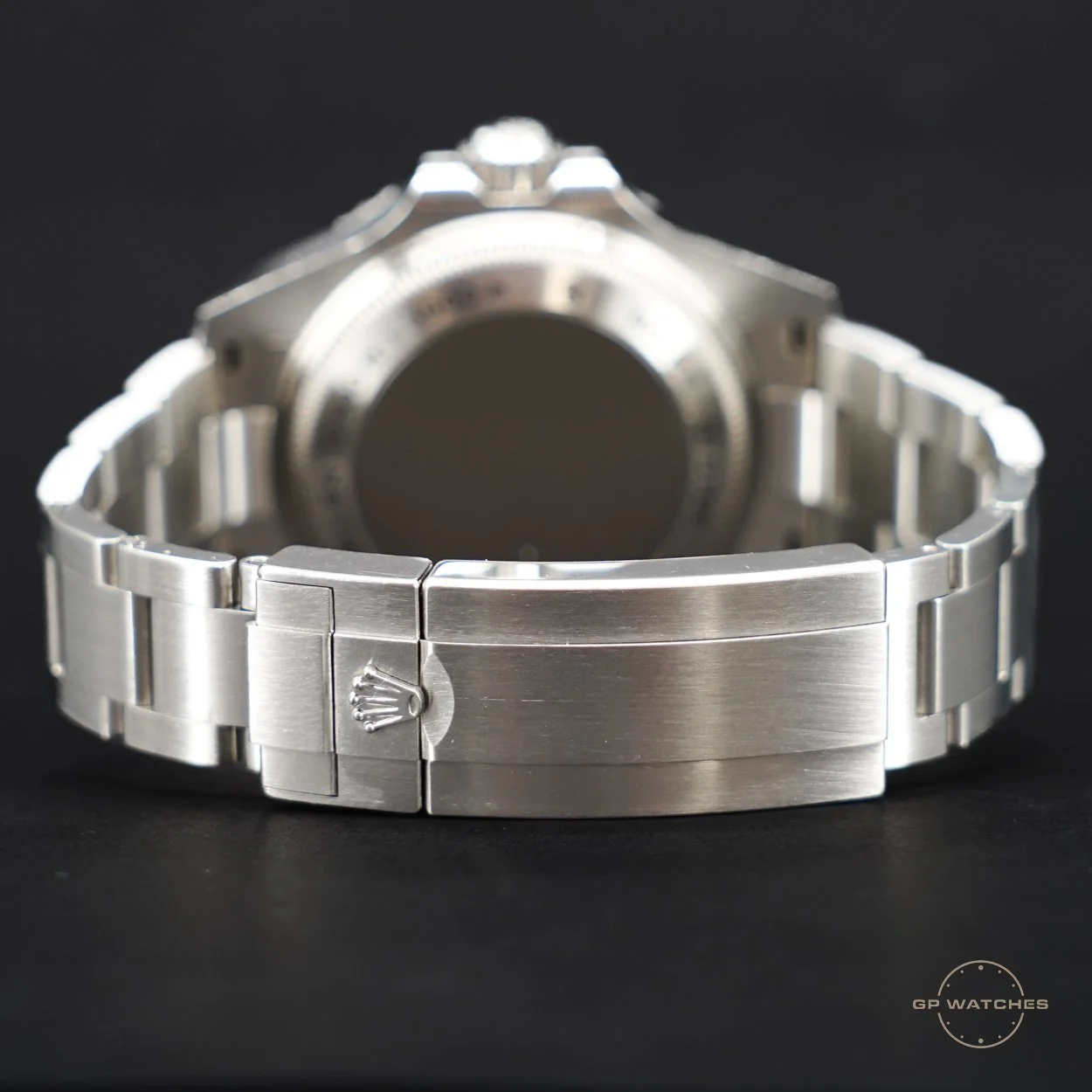 A silver metal watch with a clasp engraved with a Rolex crown, shown from the back on a black surface.