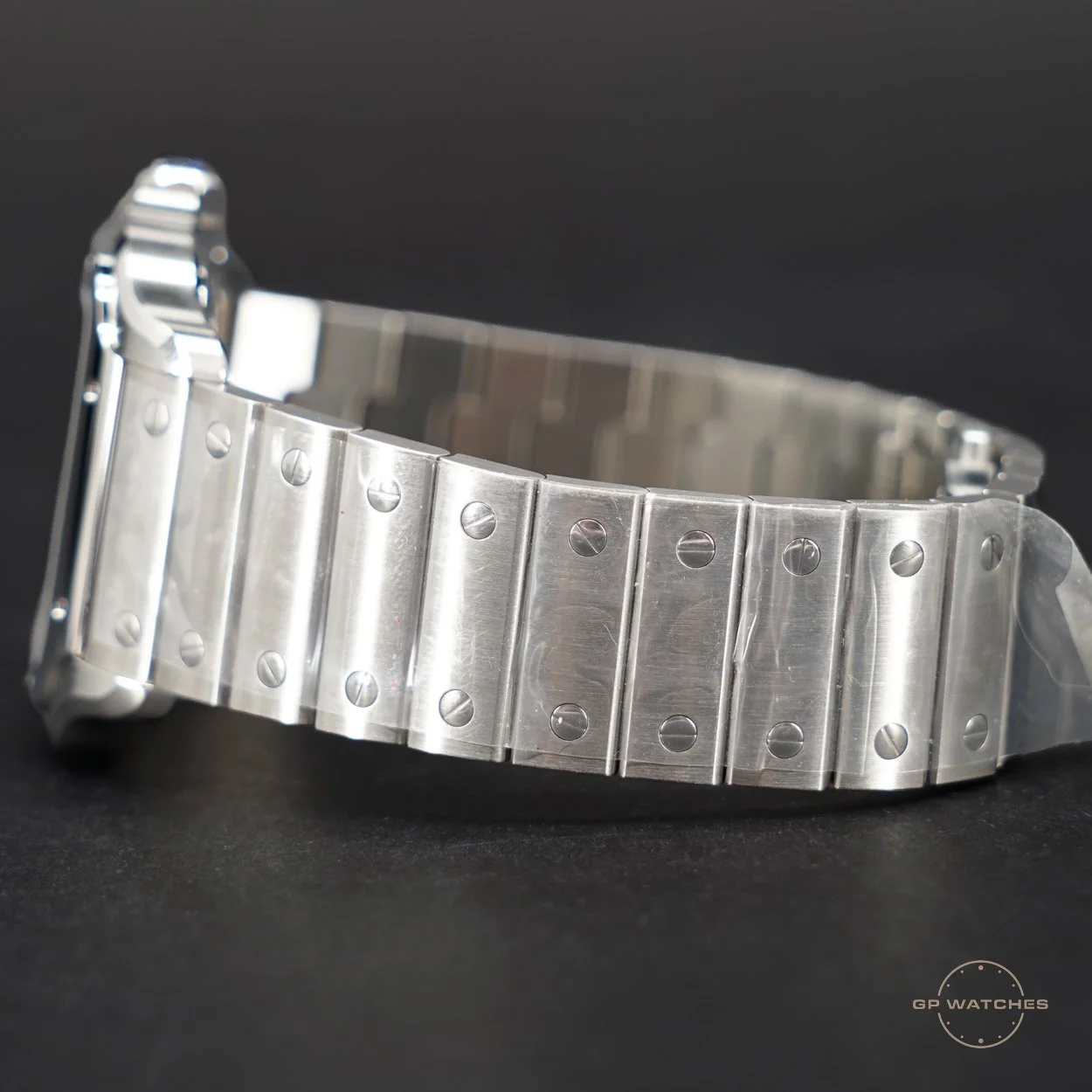 A close-up of a silver metal wristwatch band with visible screws on each link, set against a black background.