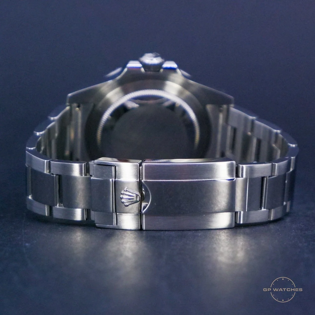 A silver wristwatch with a metal band and Rolex logo on the clasp, placed on a dark surface. The watch face is not visible.