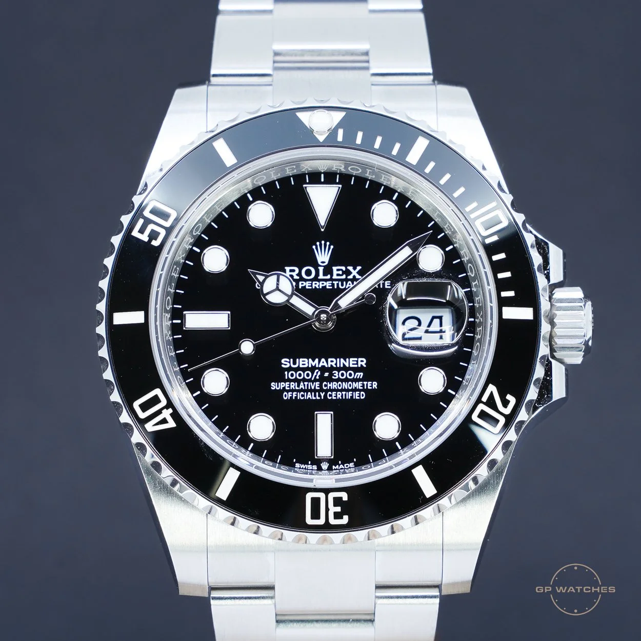 A close-up of a black and silver Rolex Submariner watch with a black dial, white markers, and a date window showing the 24th, against a dark background.