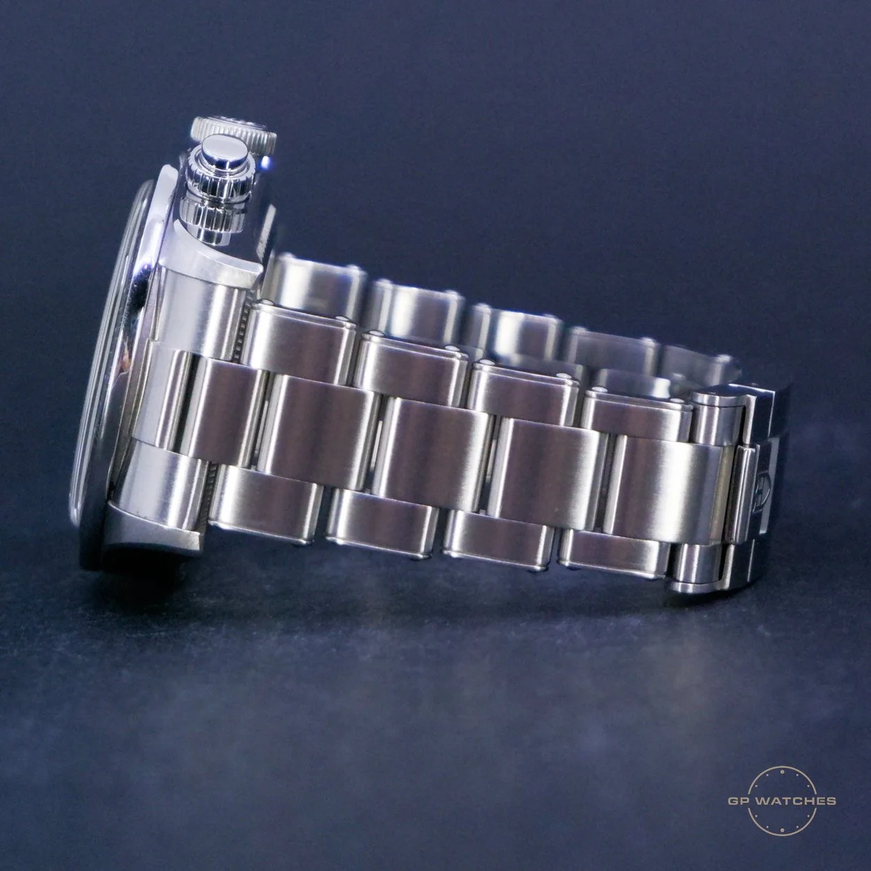 Side view of a silver stainless steel wristwatch with a metal bracelet band on a dark background.