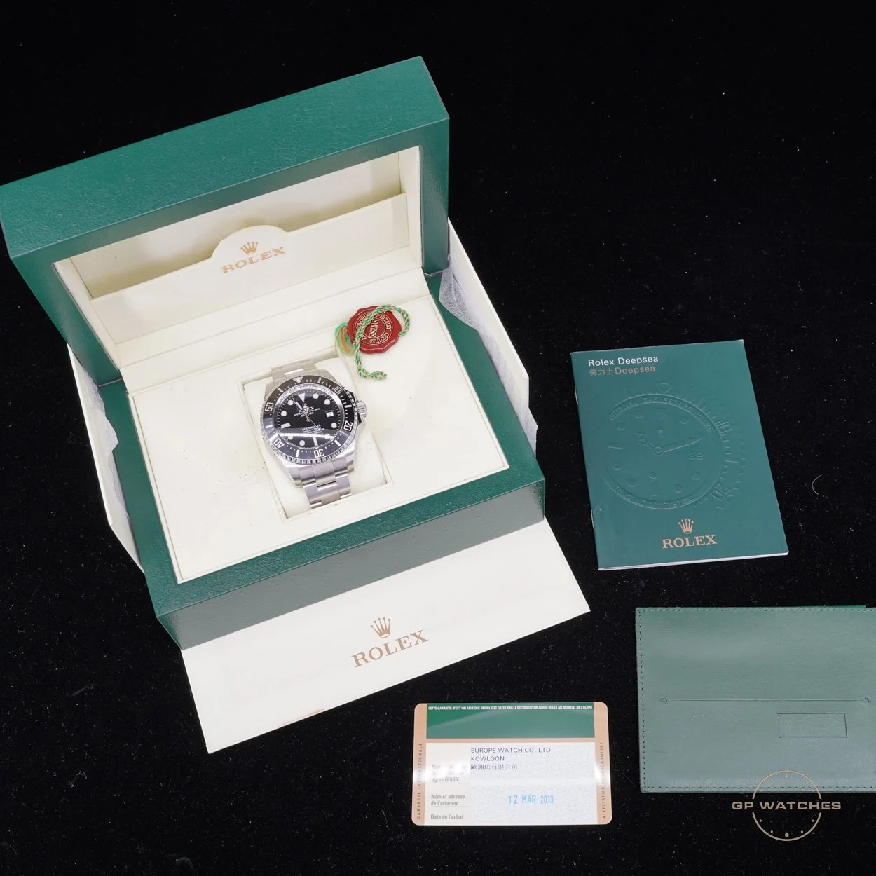 A Rolex Deepsea wristwatch in its opened green and white box, with a red and green Rolex seal attached. Next to the box are a green Rolex booklet, a green cardholder, and a card dated March 12, 2013, from Europe Watch Co. Ltd.