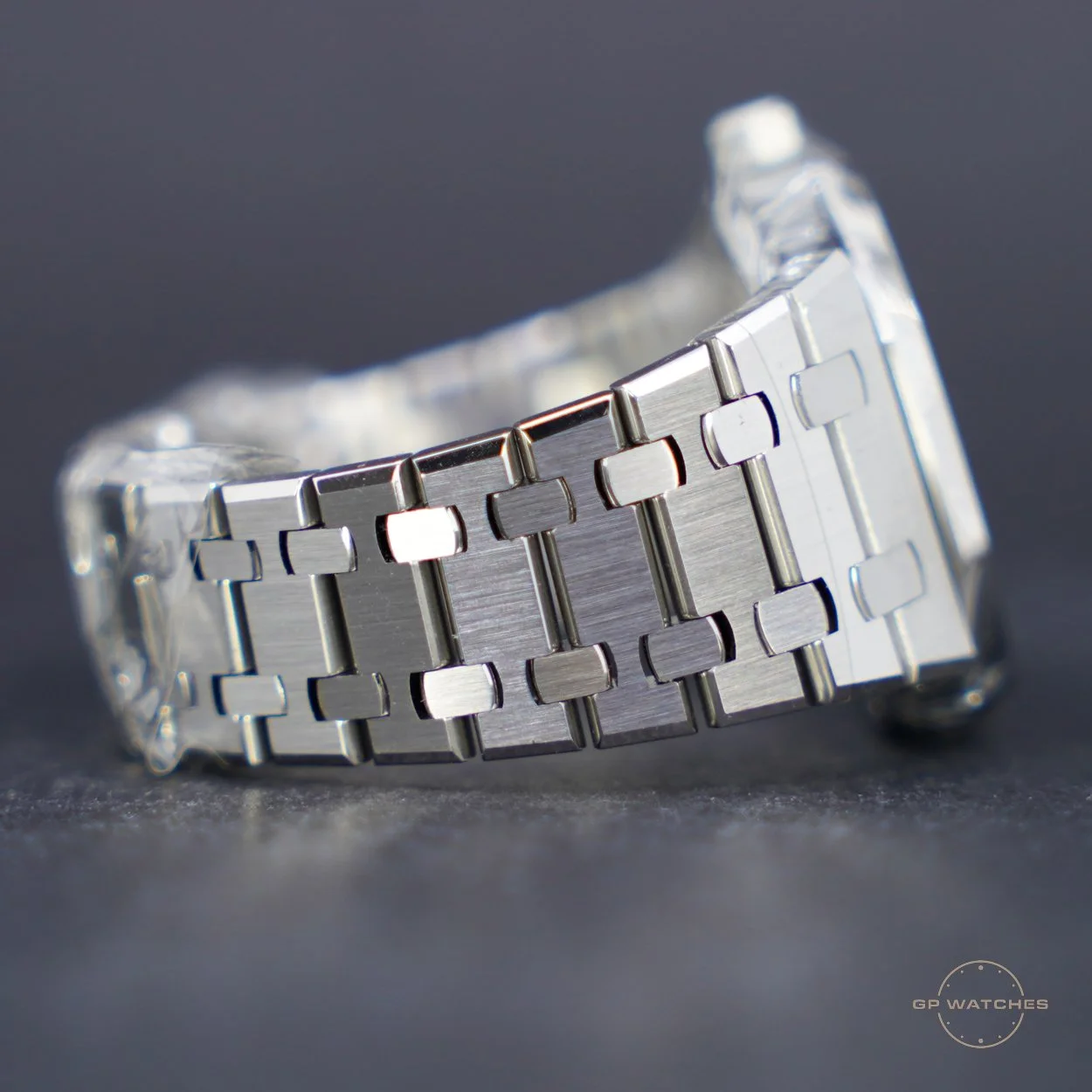 Close-up of a stainless steel wristwatch band with a brushed finish on a dark surface.