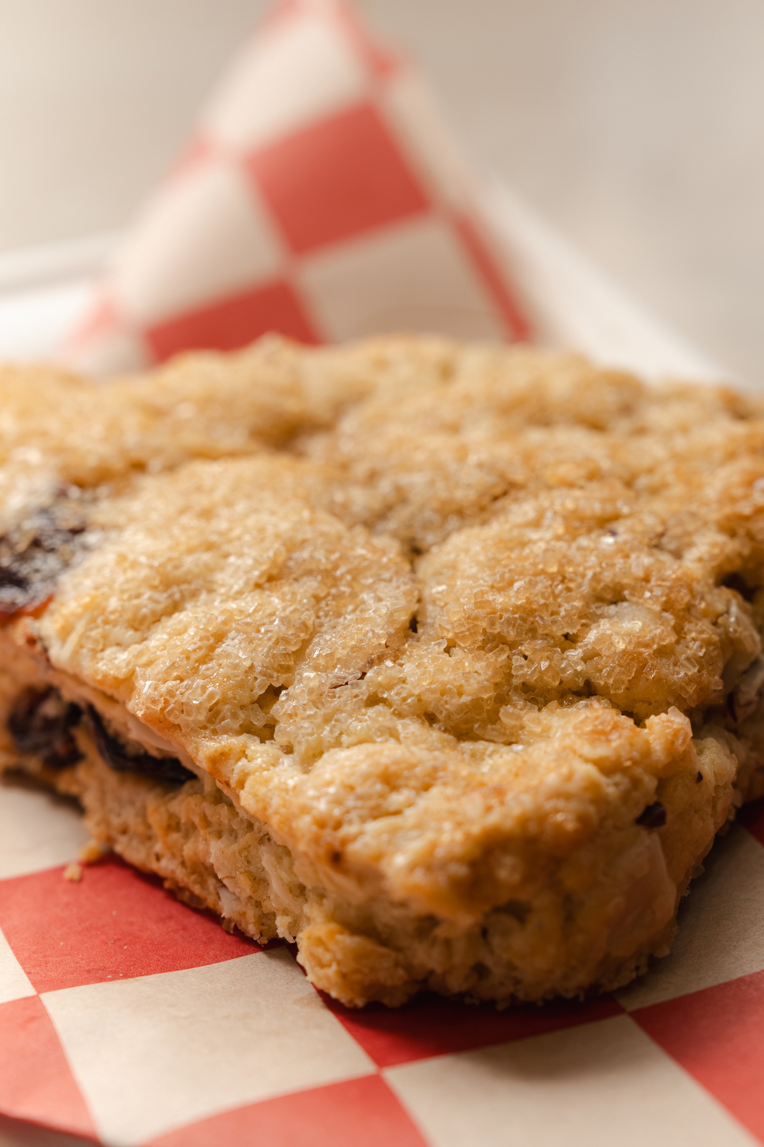 Close-up of a sugared scone on checkered paper, commercial food photography for a local bakery.