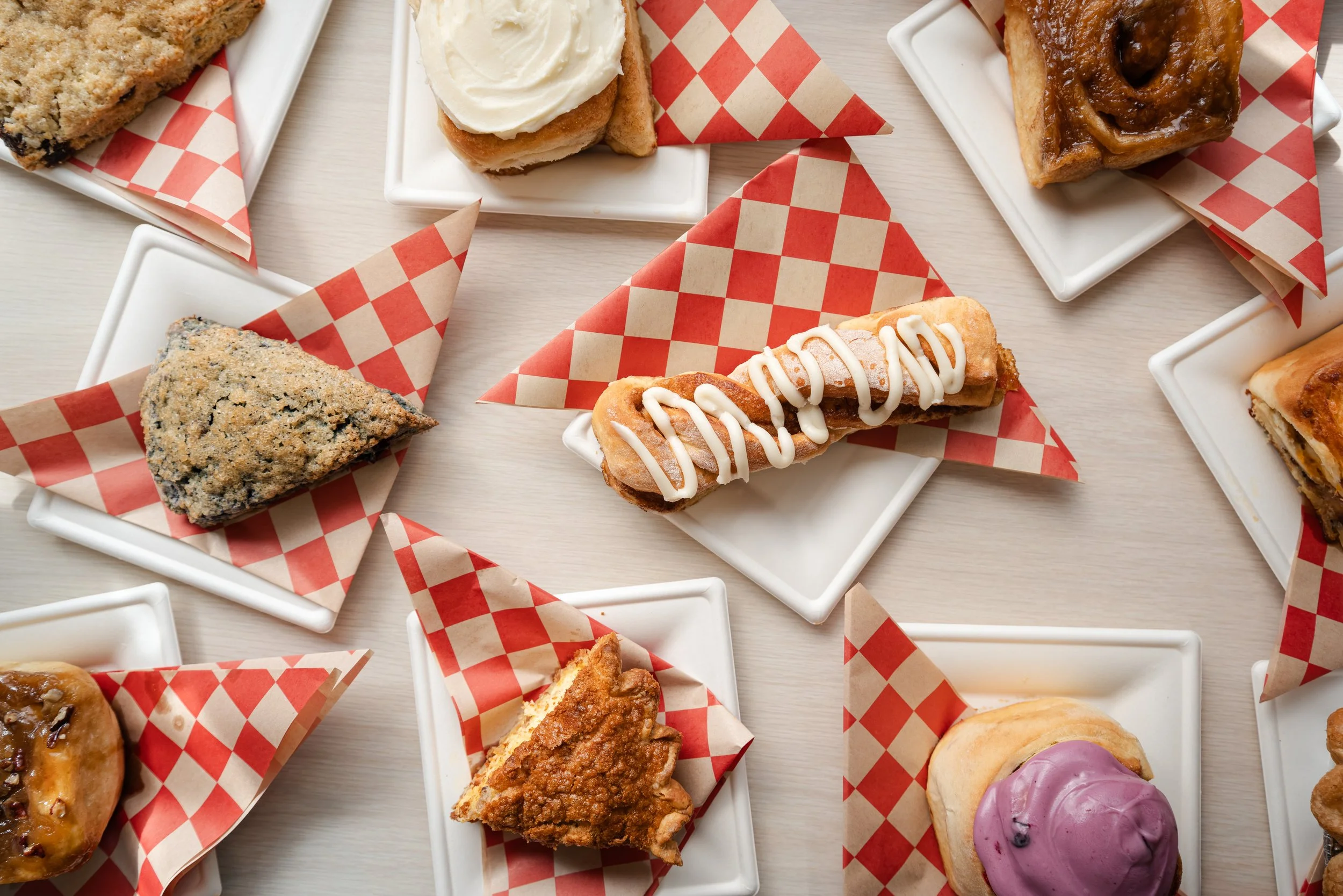 Overhead spread of scones, cinnamon rolls and hand pies on checkered paper, shot for a bakery's menu and social content