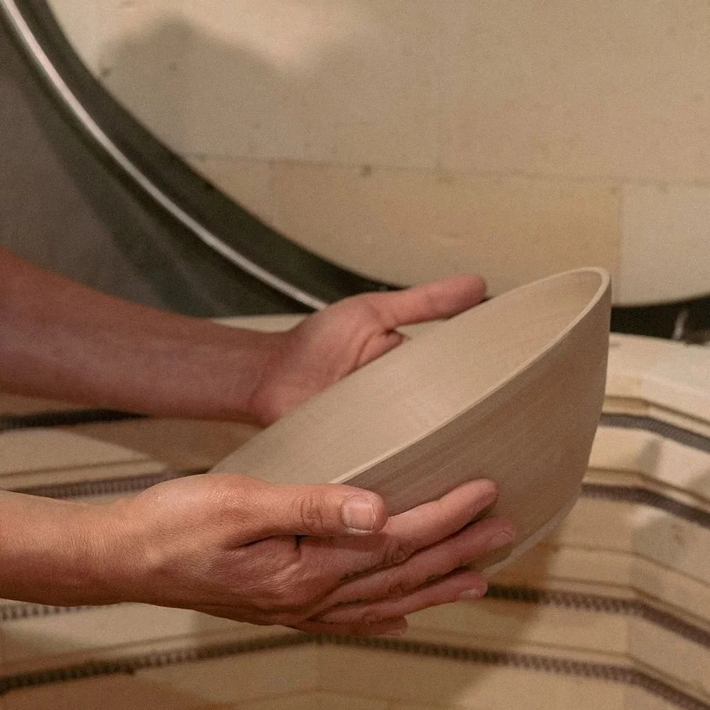 Person lifting a handmade ceramic bowl out of the kiln.