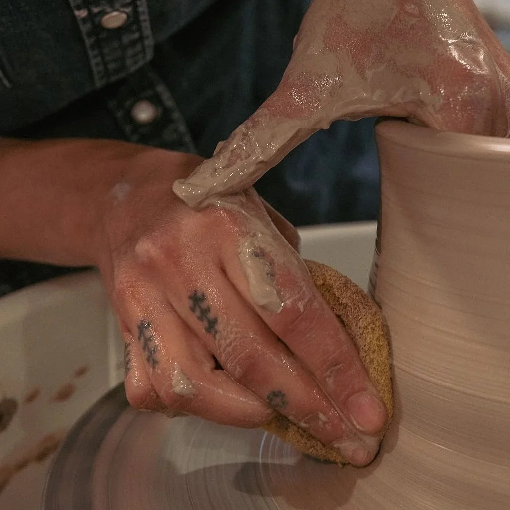 Person throwing a tall ceramic cyclinder on a pottery wheel.