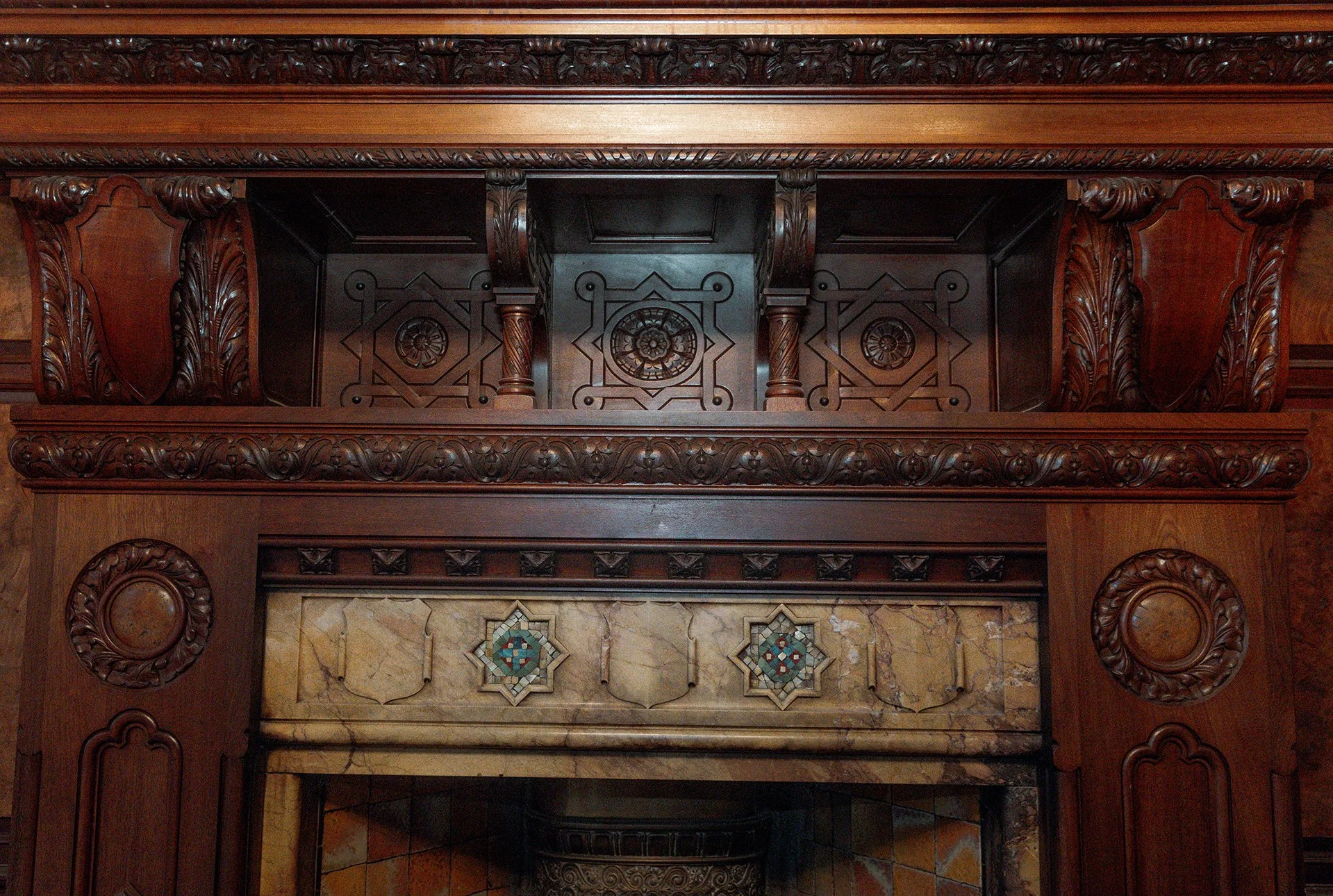 Wooden fireplace mantel with intricate carvings and decorative tiles.