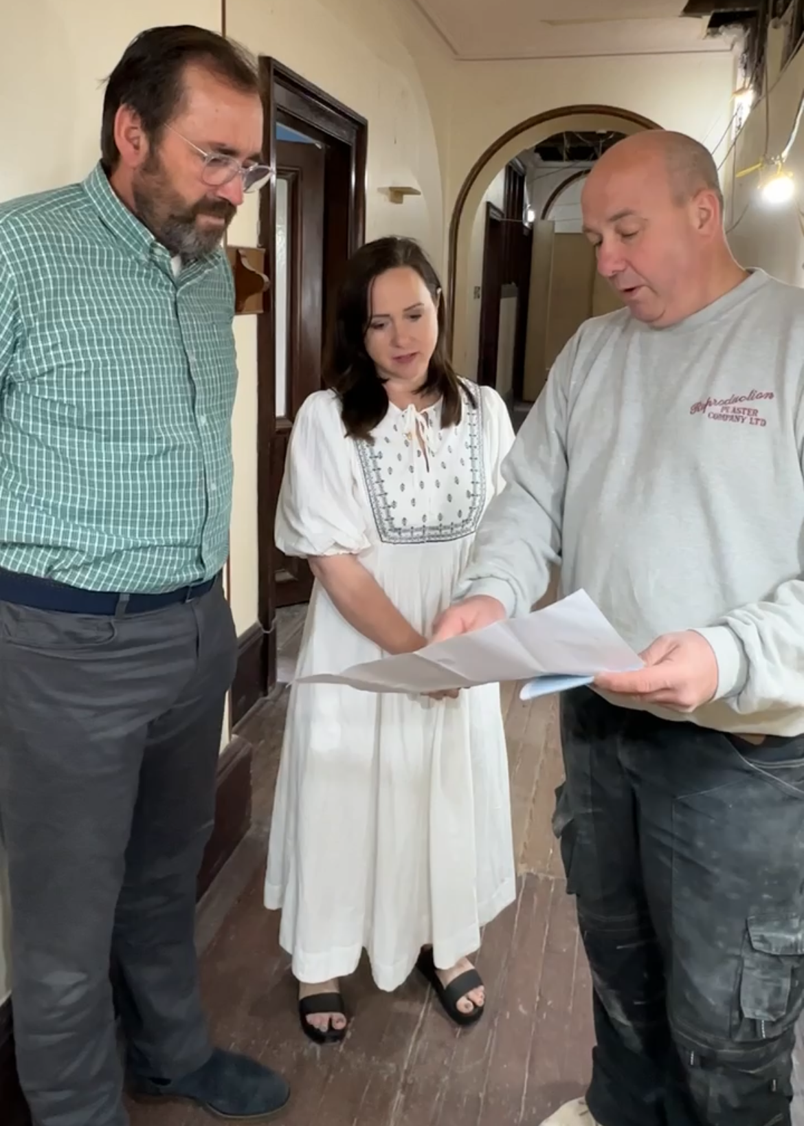 Three people reviewing documents together in an indoor setting, with two men and a woman standing closely.