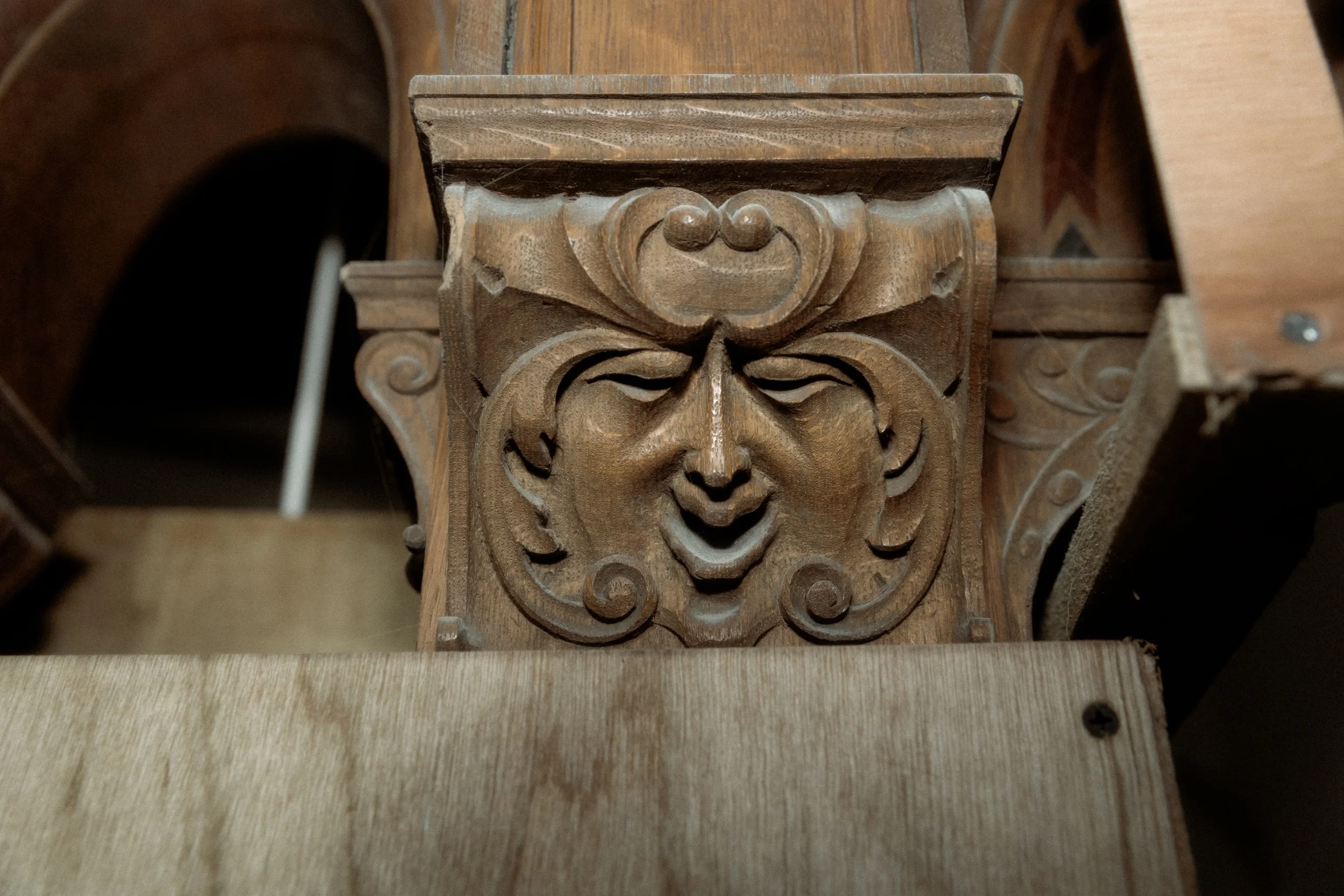 Close-up of carved wooden architectural detail featuring a face with a smiling expression and decorative scrolls.