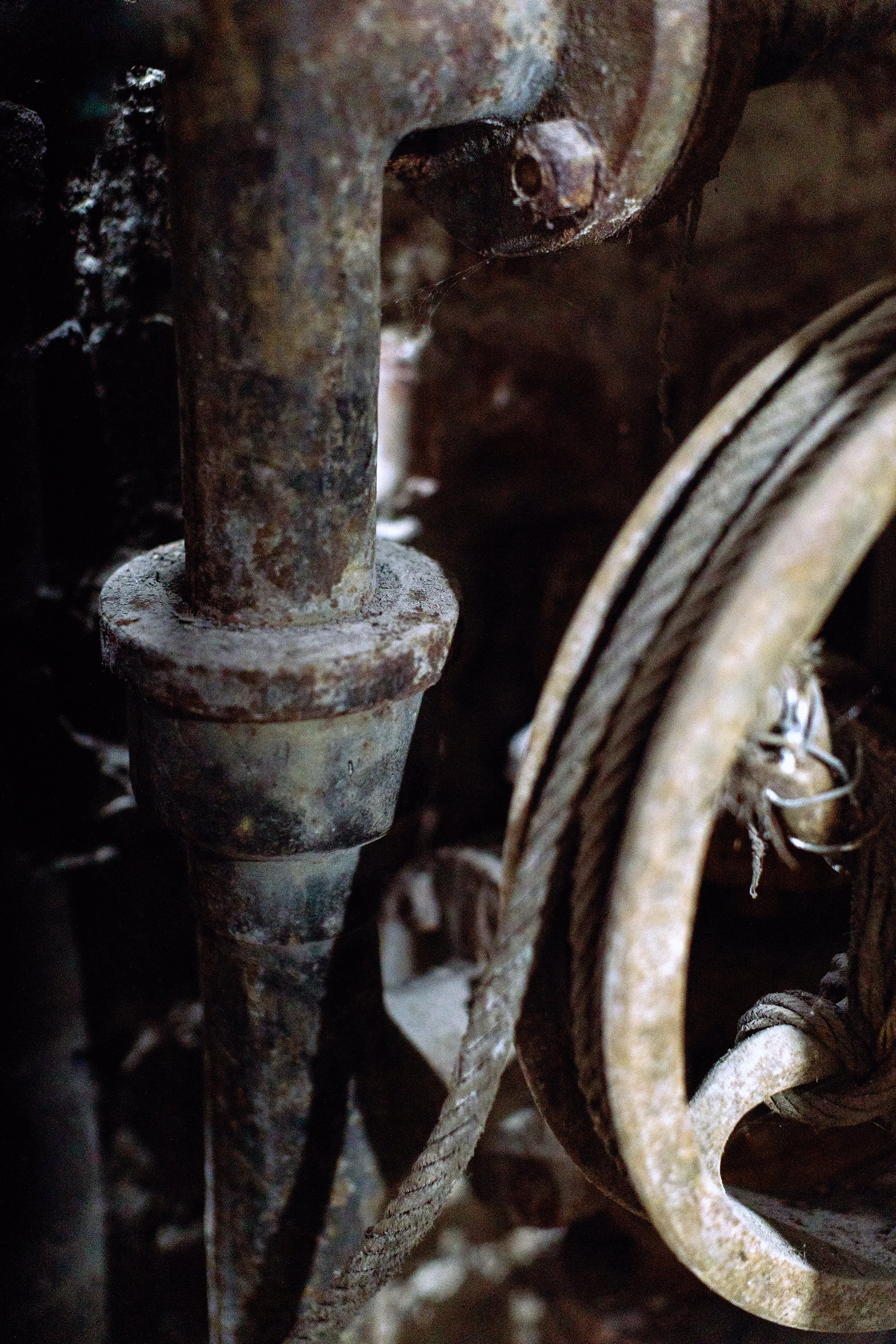 Close-up of rusted metal machinery and a rope in a dark, dusty setting.