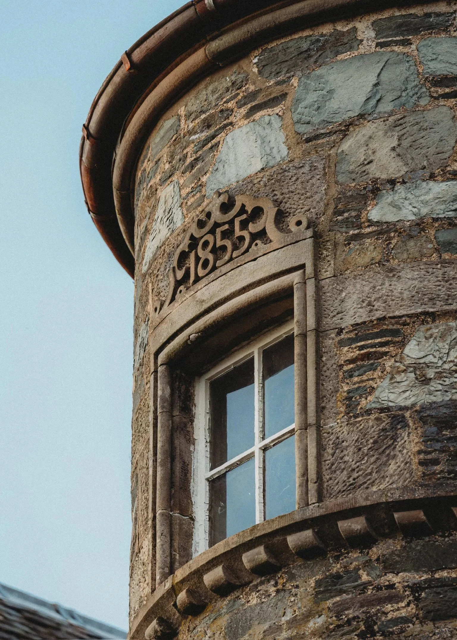 A close-up view of a historic stone building with a decorative stone plaque displaying the year 1855 above a small white window on a stone wall.