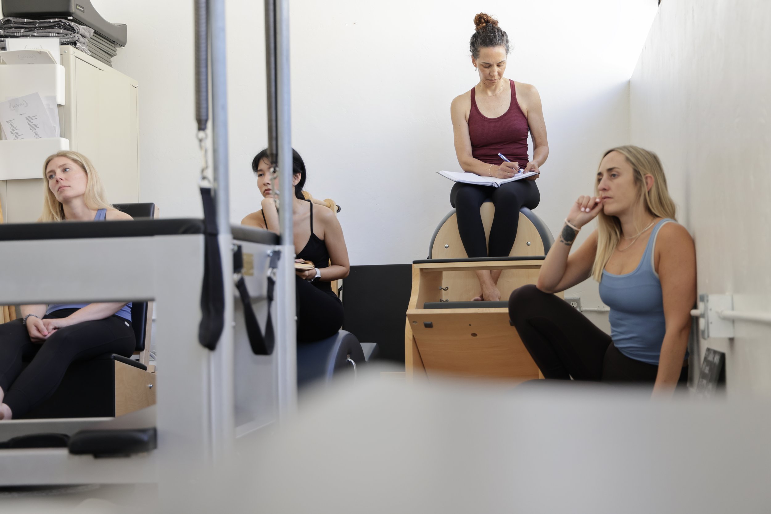 Our founders, sitting on the floor in the Pilates Studio, Michelle is smiling at the camera, and Nicole is looking at Michelle.