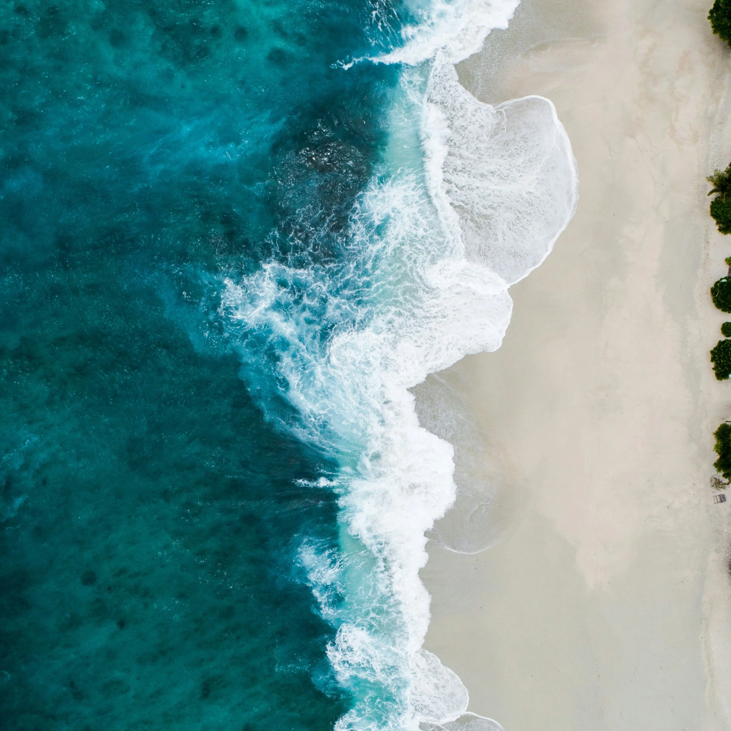 Aerial view of waves crashing onto a sandy beach with turquoise water and light surf.