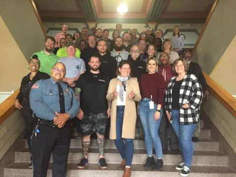 Group of people posing on stairs, some in casual and some in uniform, indoors.