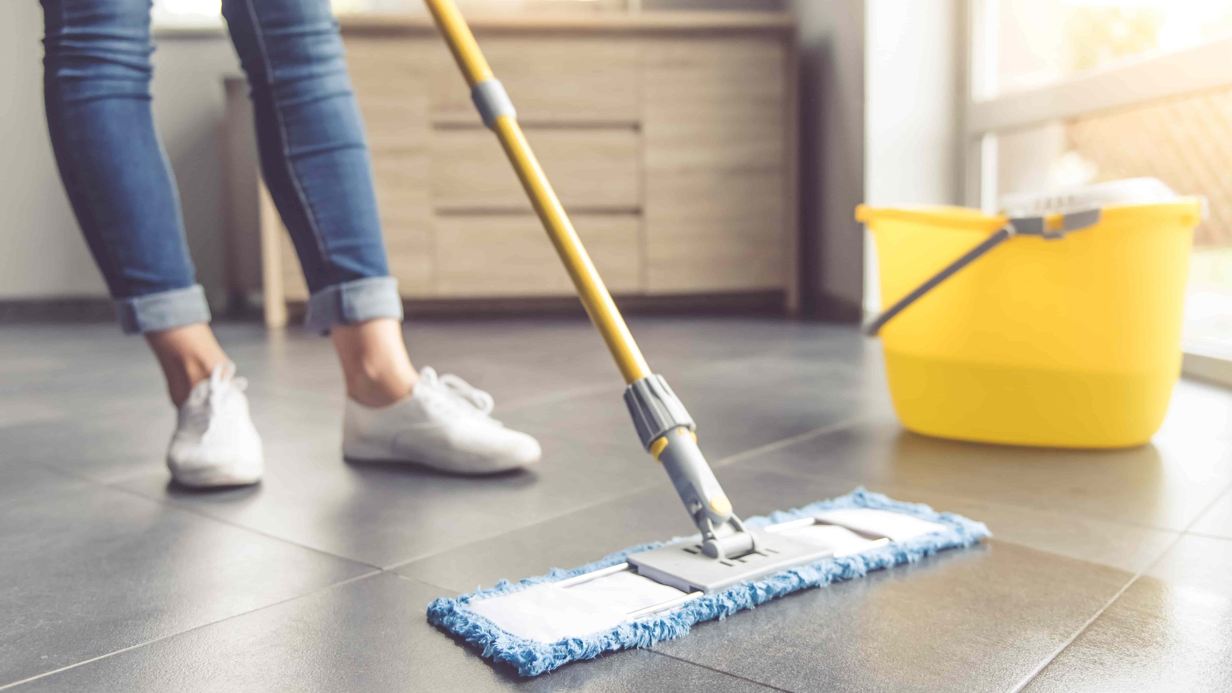 Person mopping a tile floor with a yellow mop and bucket.