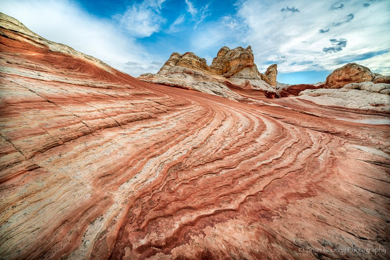 Colorful layered sandstone formations in a desert landscape under a partly cloudy sky.