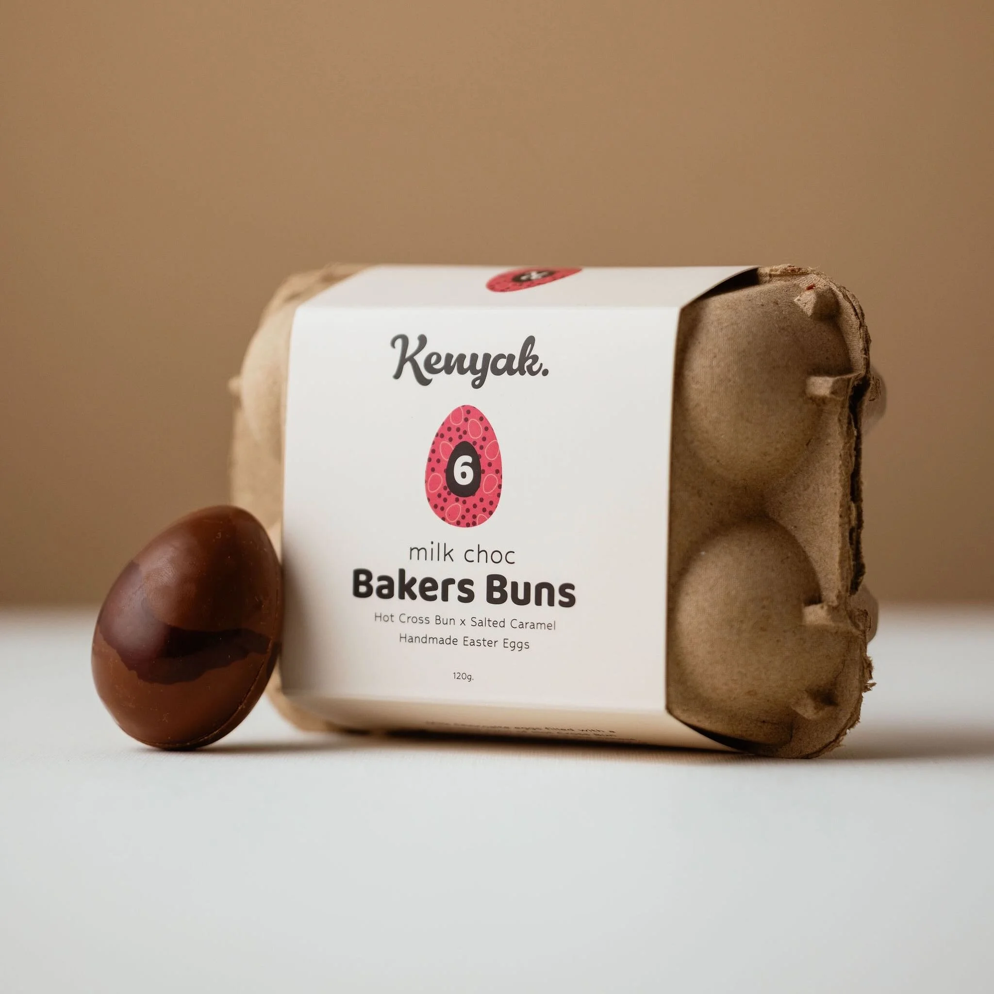 Chocolate egg and a carton of Kenyak milk chocolate Bakers Buns with Easter eggs on white background.