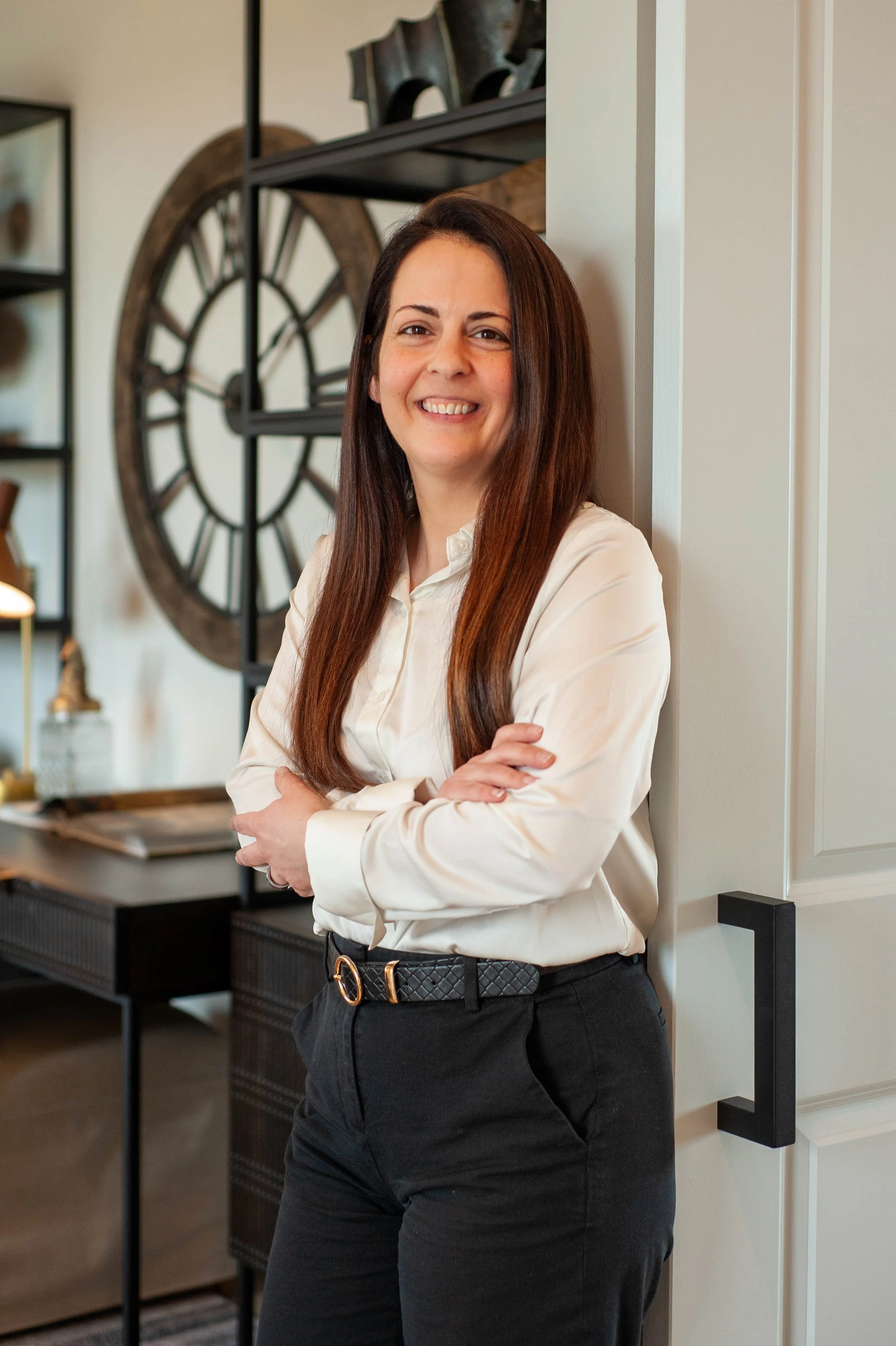 A woman with long brown hair smiling while leaning against a barn door leading to an office.