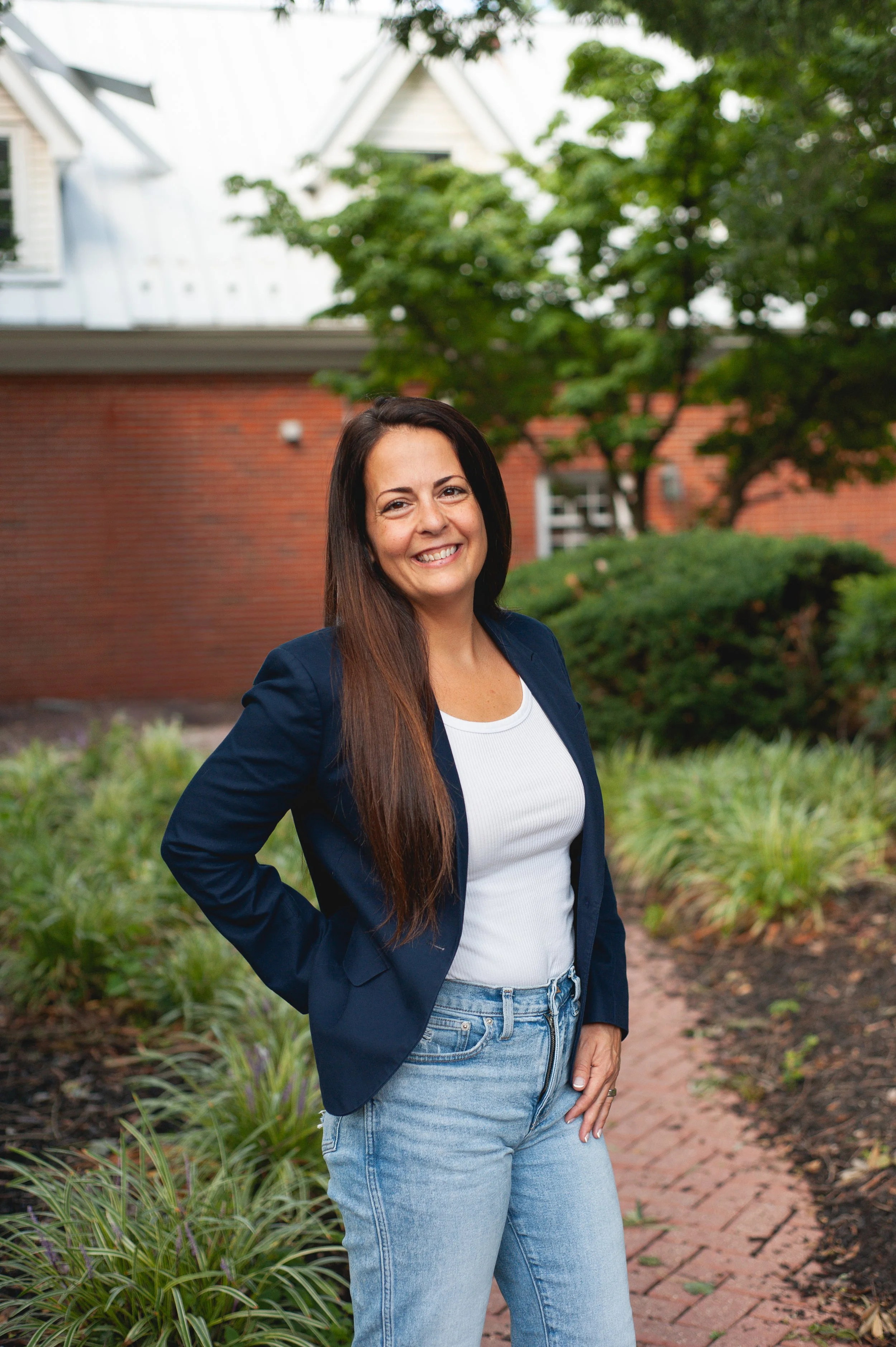 A woman with long brown hair smiling while leaning against a barn door leading to an office.