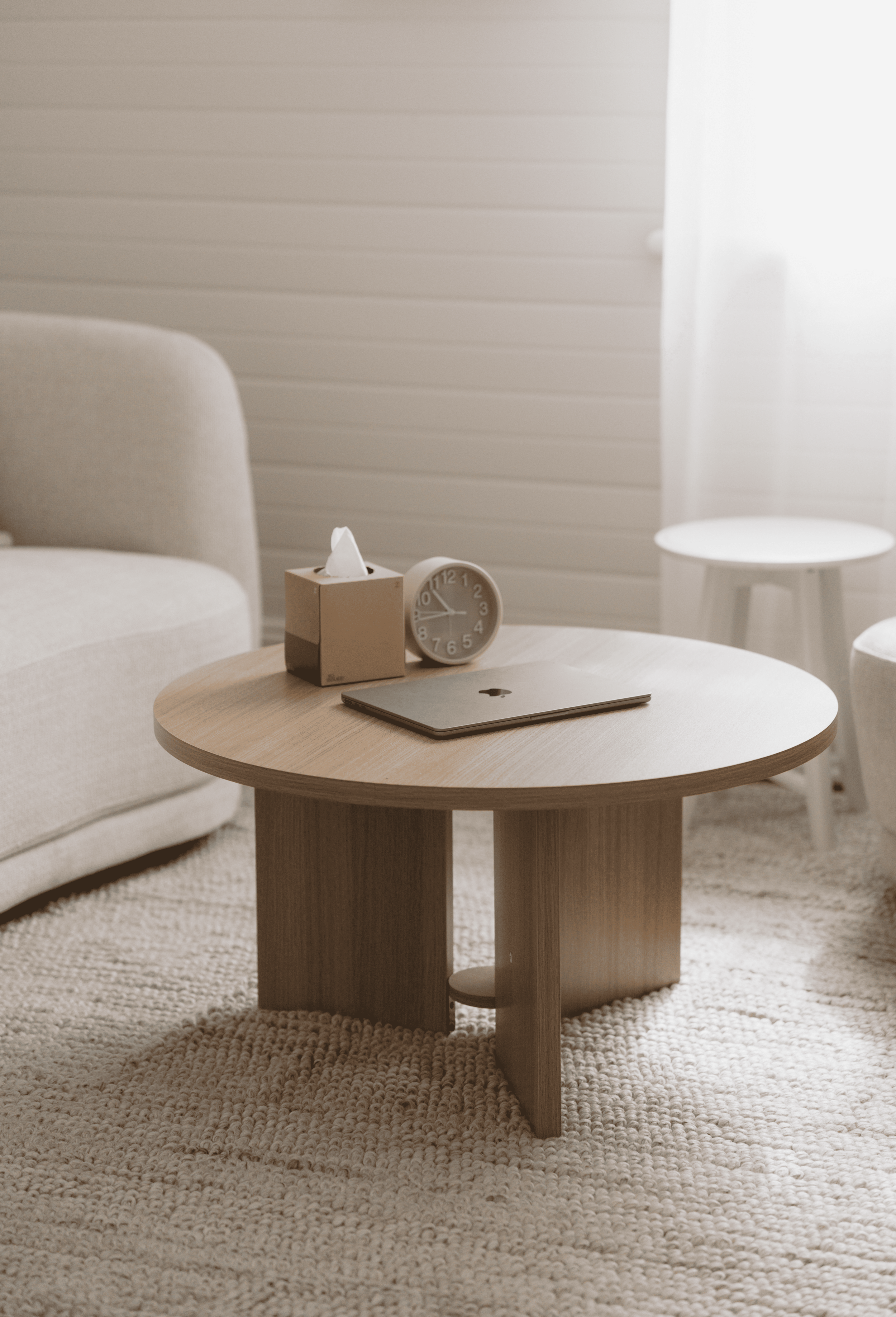 A laptop, tissue box, and clock on a wooden table setup for an online therapy australia or telehealth session.