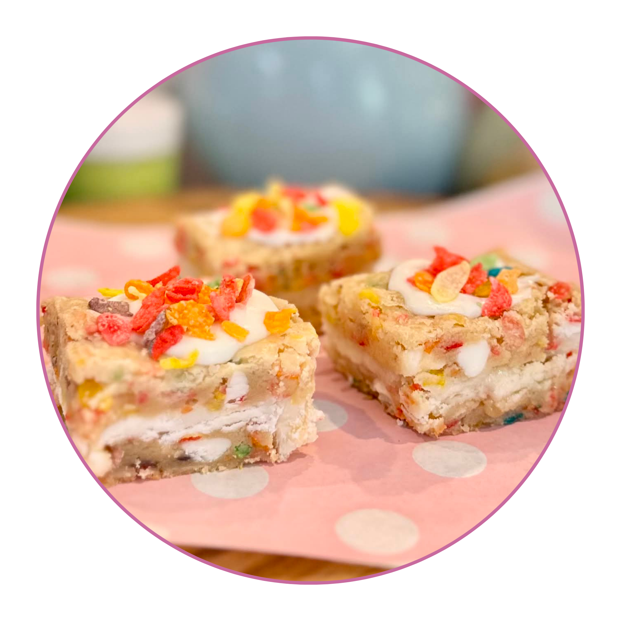 Close-up of three vanilla frosted cookies topped with colorful cereal pieces on pink polka dot paper.