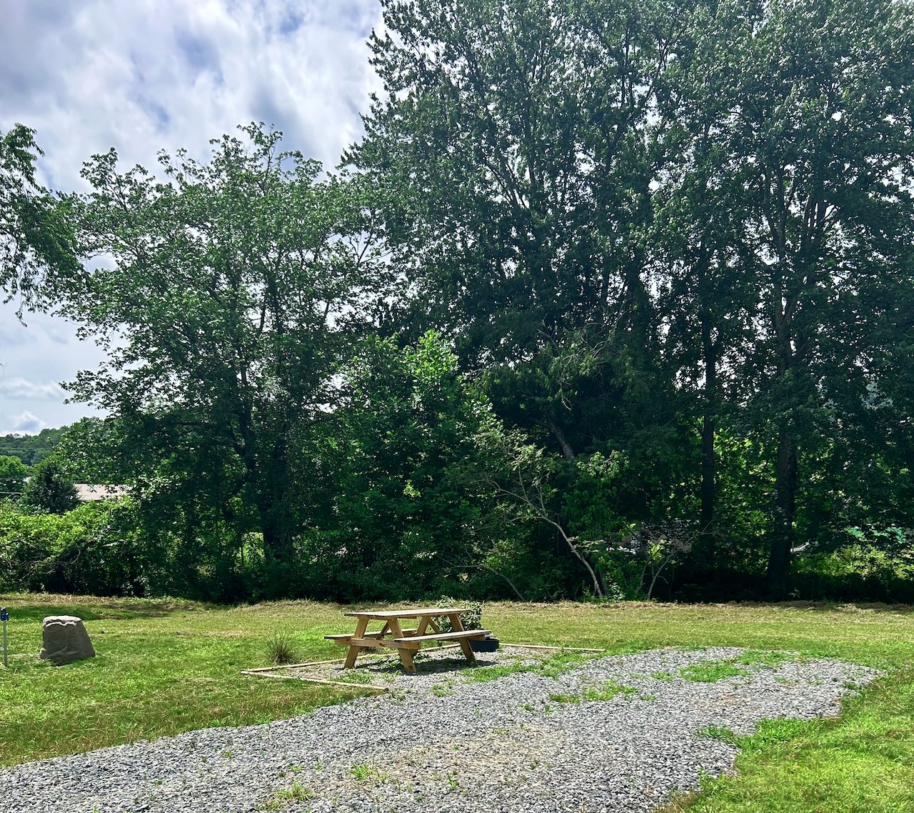 A picnic table on a grassy area with trees in the background and a partly cloudy sky.