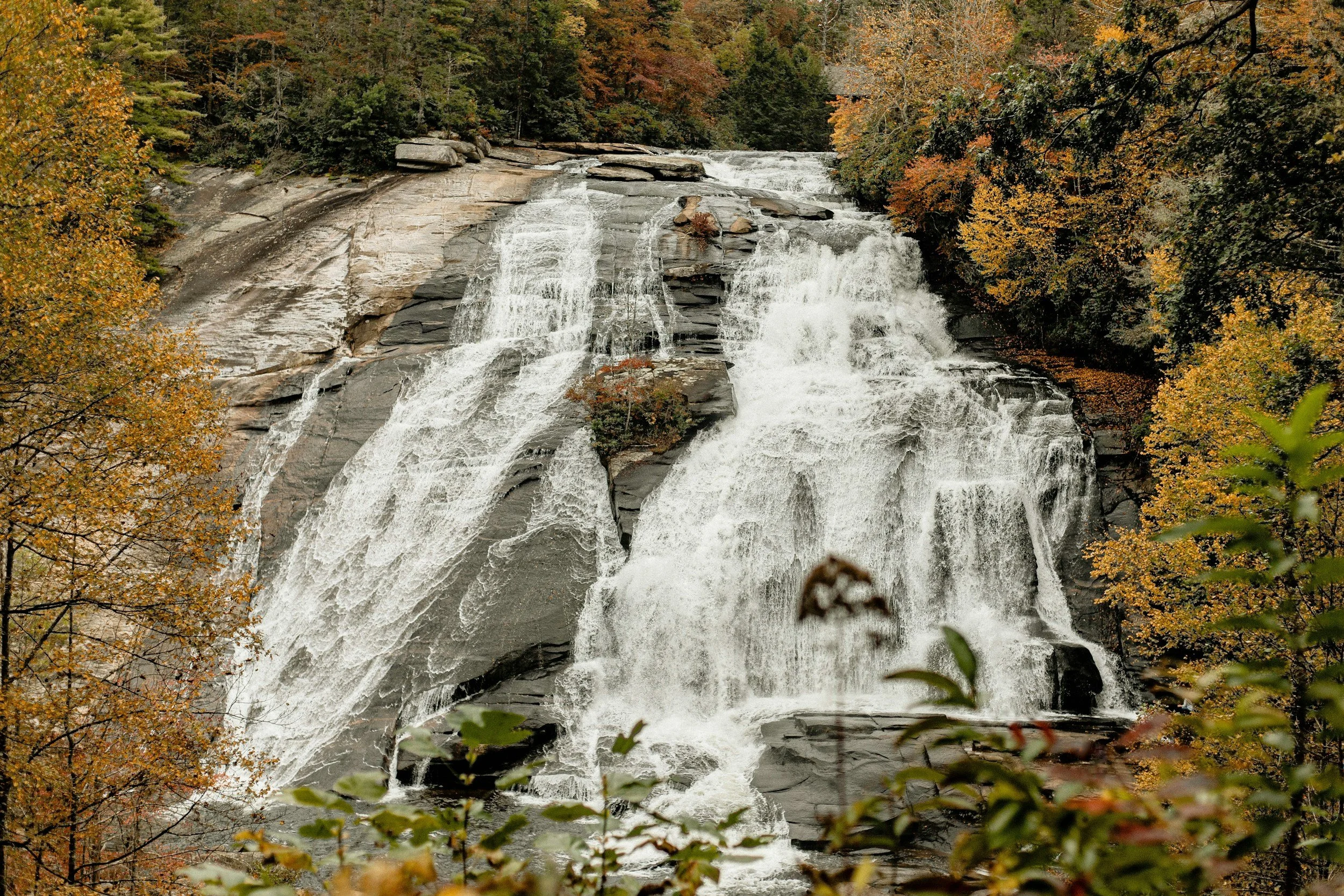 A waterfalls cascading down a rocky cliff surrounded by trees with autumn foliage.