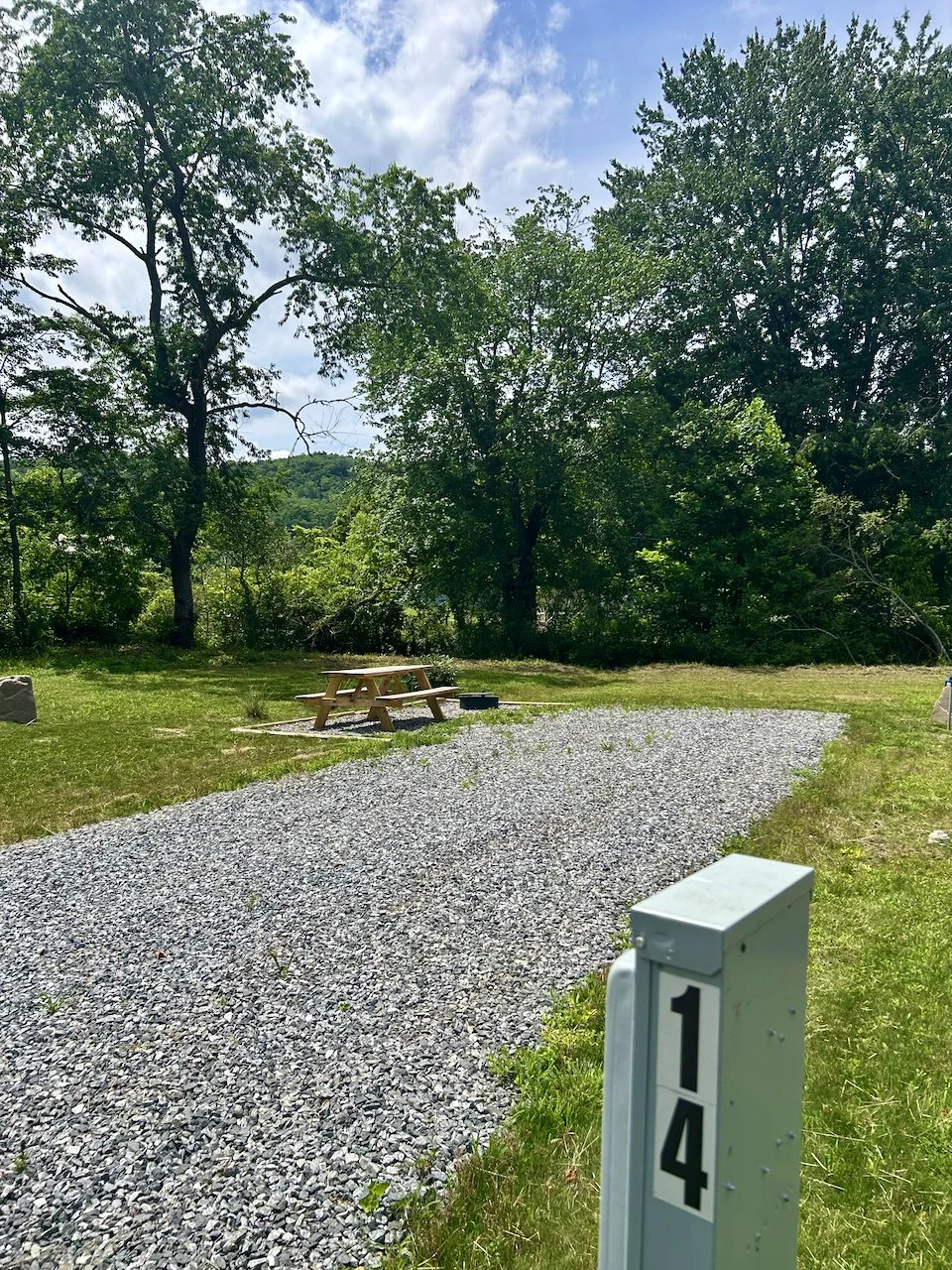 A gravel path leading to a picnic table and surrounded by green trees in a park.