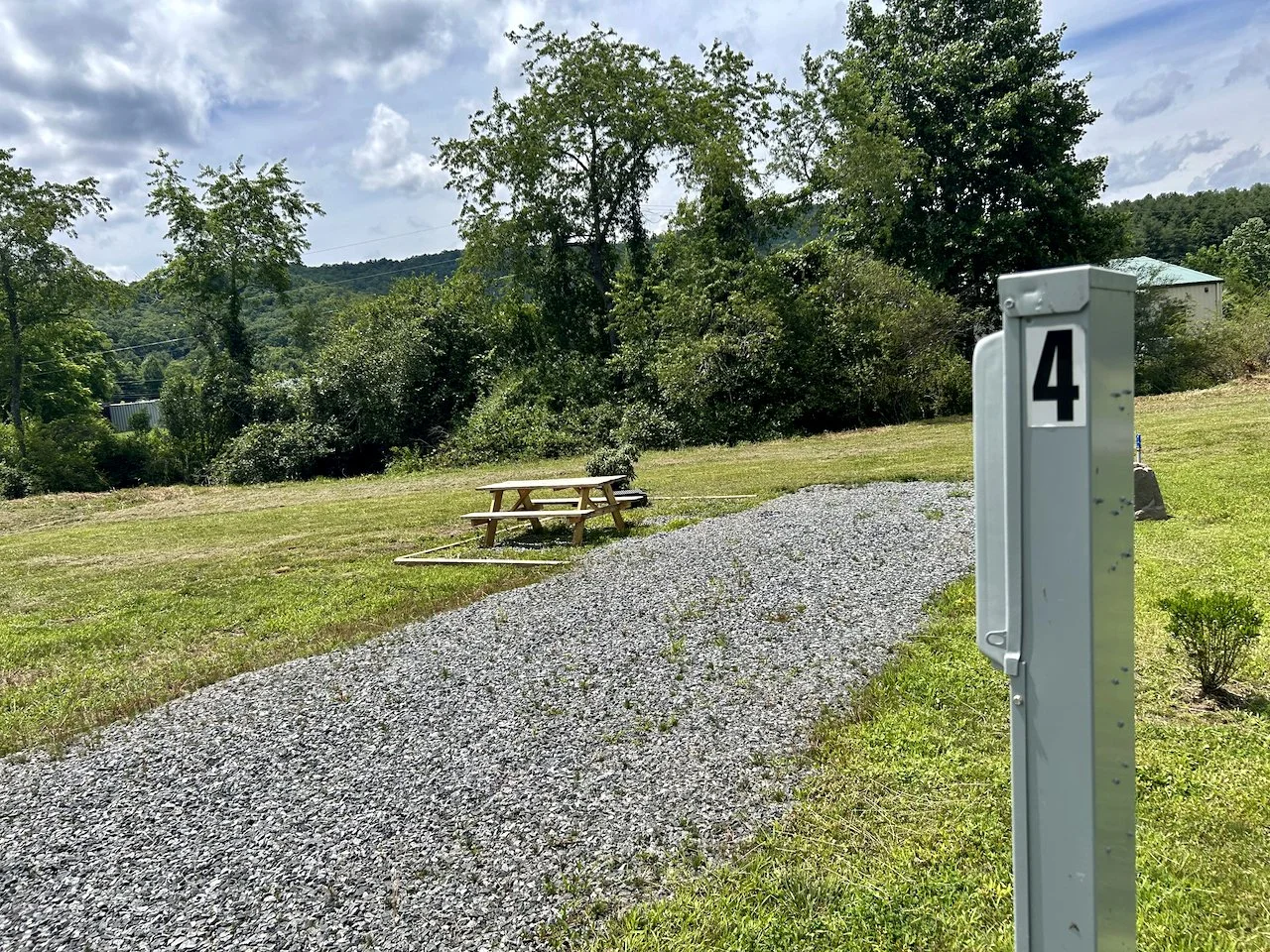 A gravel path leading to a picnic table on a grassy area with trees and a house in the background. A metal post with the number 4 is in the foreground.