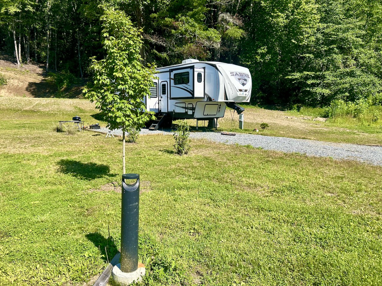 A white RV parked on a gravel driveway in a grassy, wooded area with trees in the background.