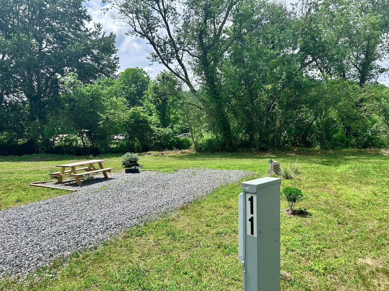 A grassy backyard with a gravel pathway, a picnic table, a potted plant, a utility box labeled '111', and trees in the background.