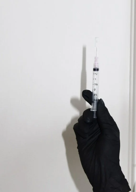 A woman touching her neck with a neutral expression, and a large syringe filled with yellow liquid floating beside her.