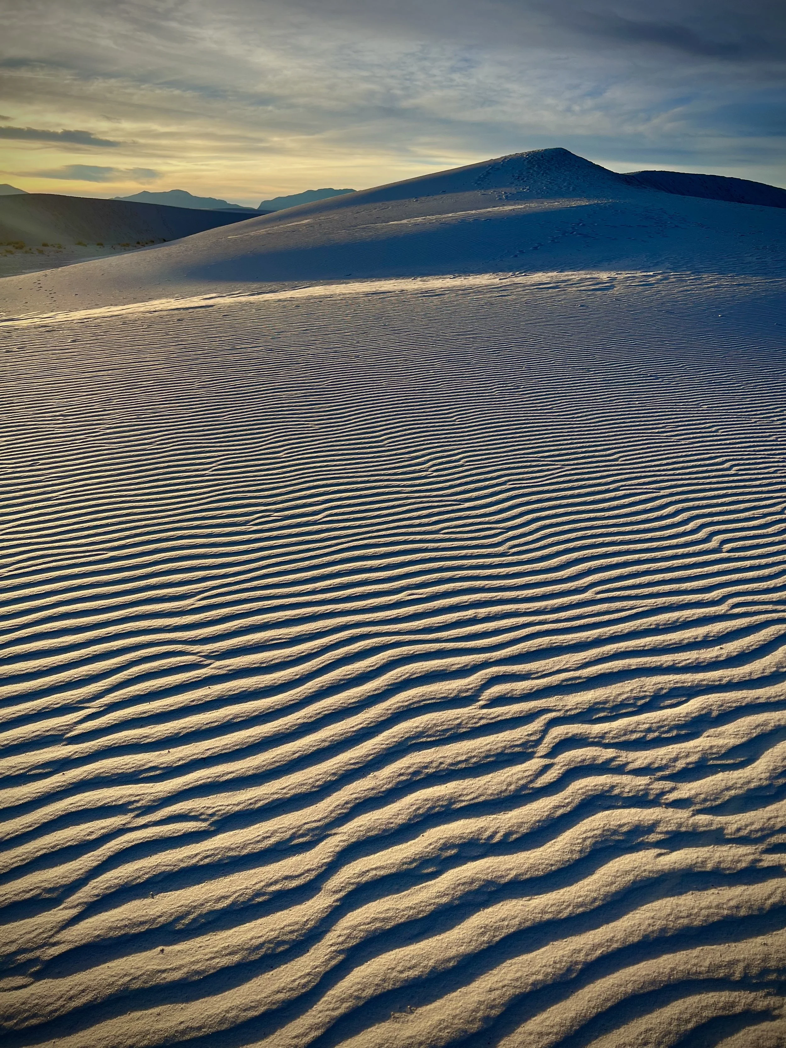 Sand dunes with rippled surface under a partly cloudy sky during sunset or sunrise signaling space.