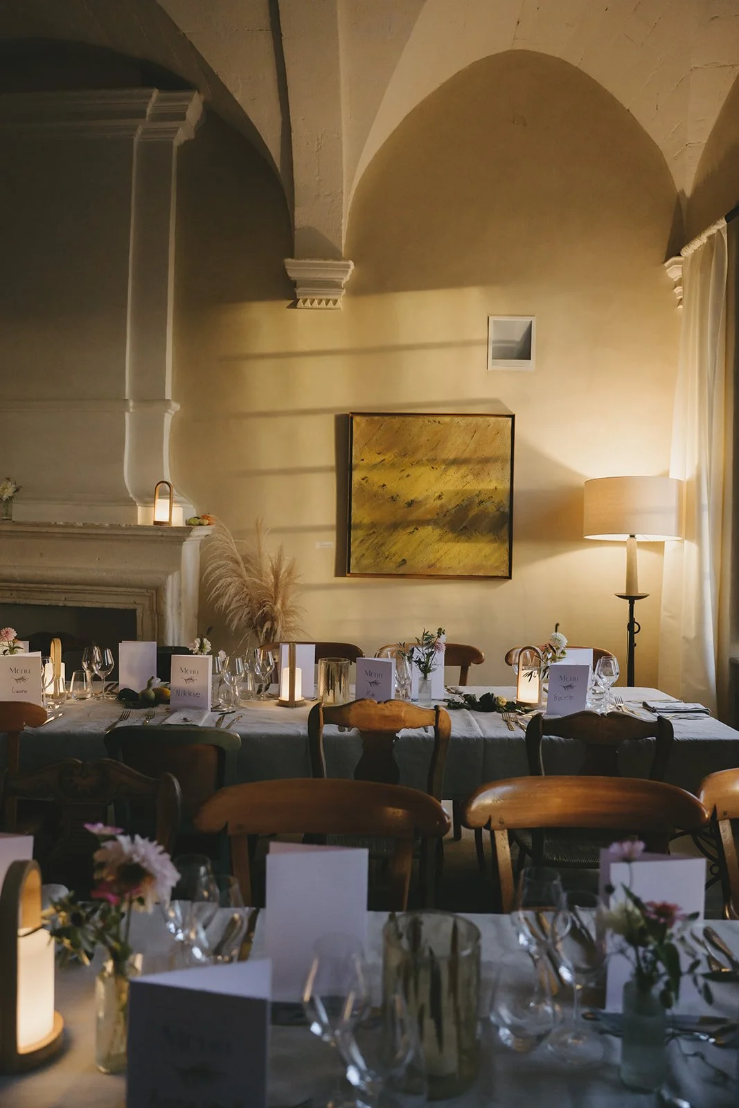 Elegant dining room set for a formal event, decorated with candles, roses, and place cards, with warm lighting and a fireplace.