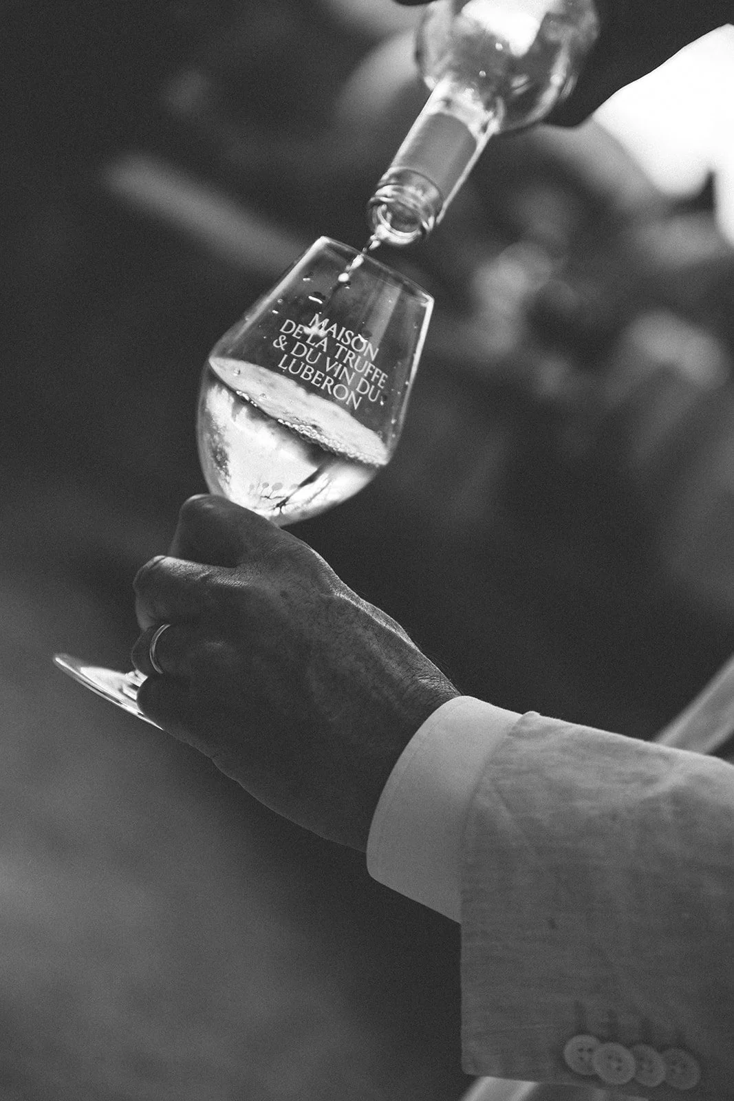 A person in a suit pours wine into a glass labeled 'Maison de la Truffe & du Vin du Luberon.'