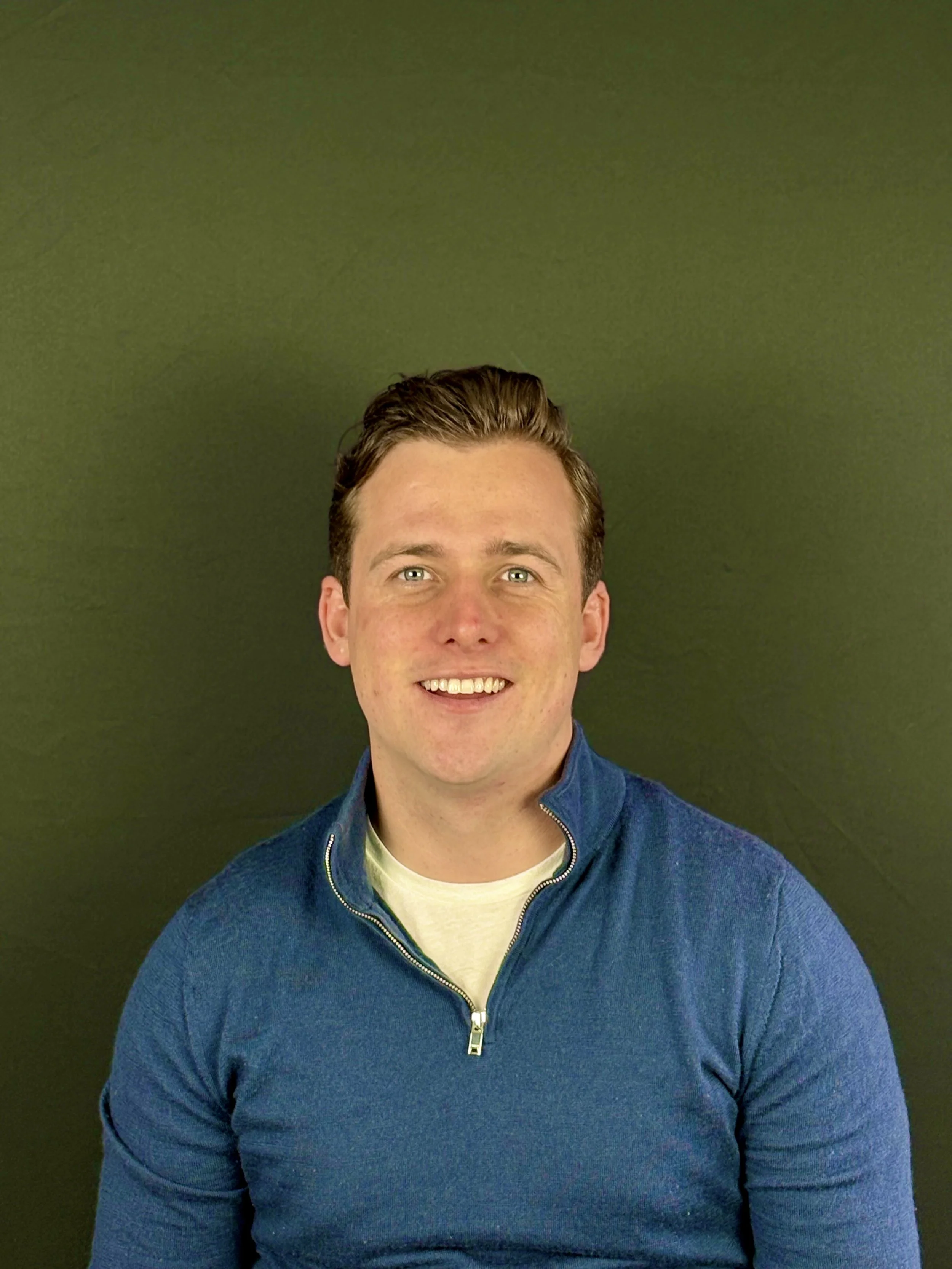 Smiling person wearing a blue sweater against a green background.