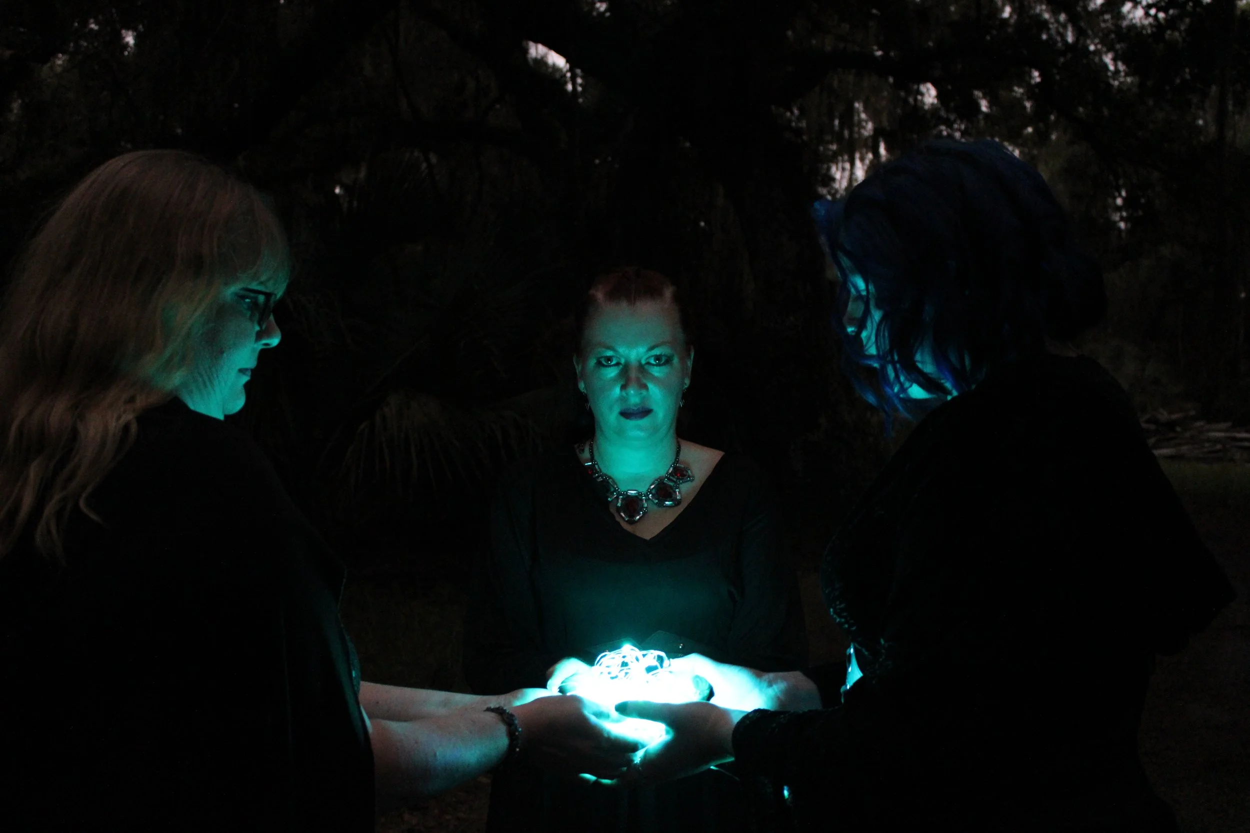 Three women dresssed as witches summon a ball of light