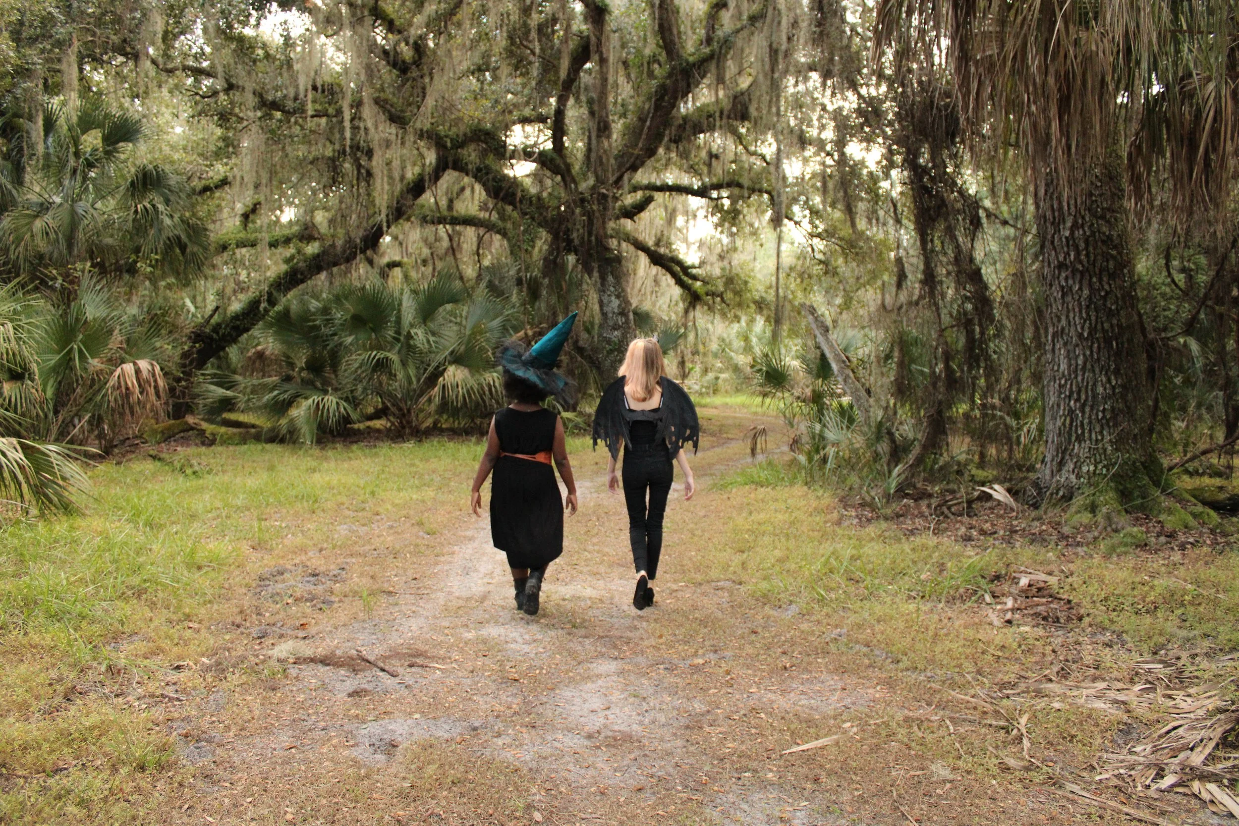 a girl dressed as a demon and a girl dressed as a witch walk into the woods