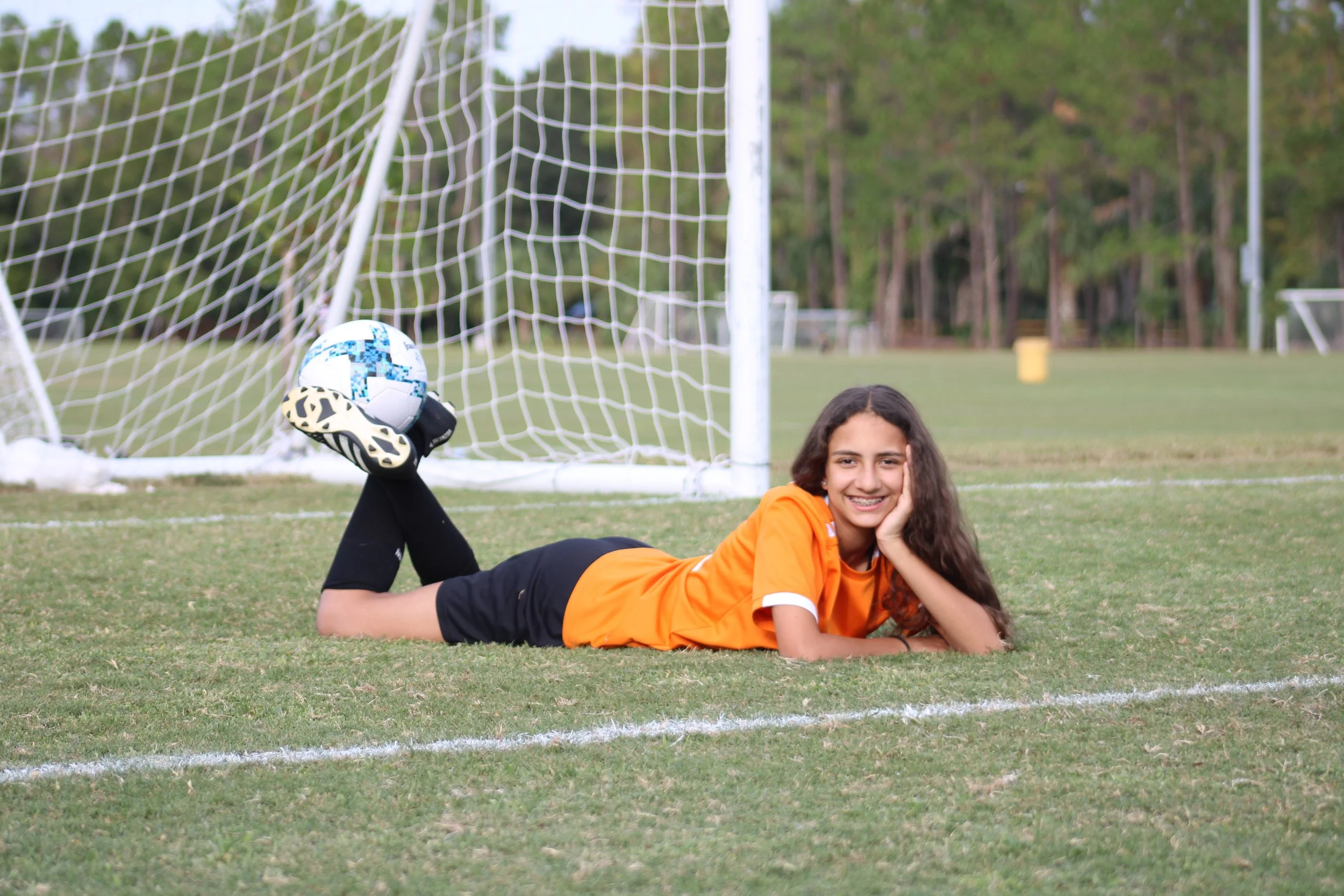 Young soccer player laying on the field holding the ball with her feet.