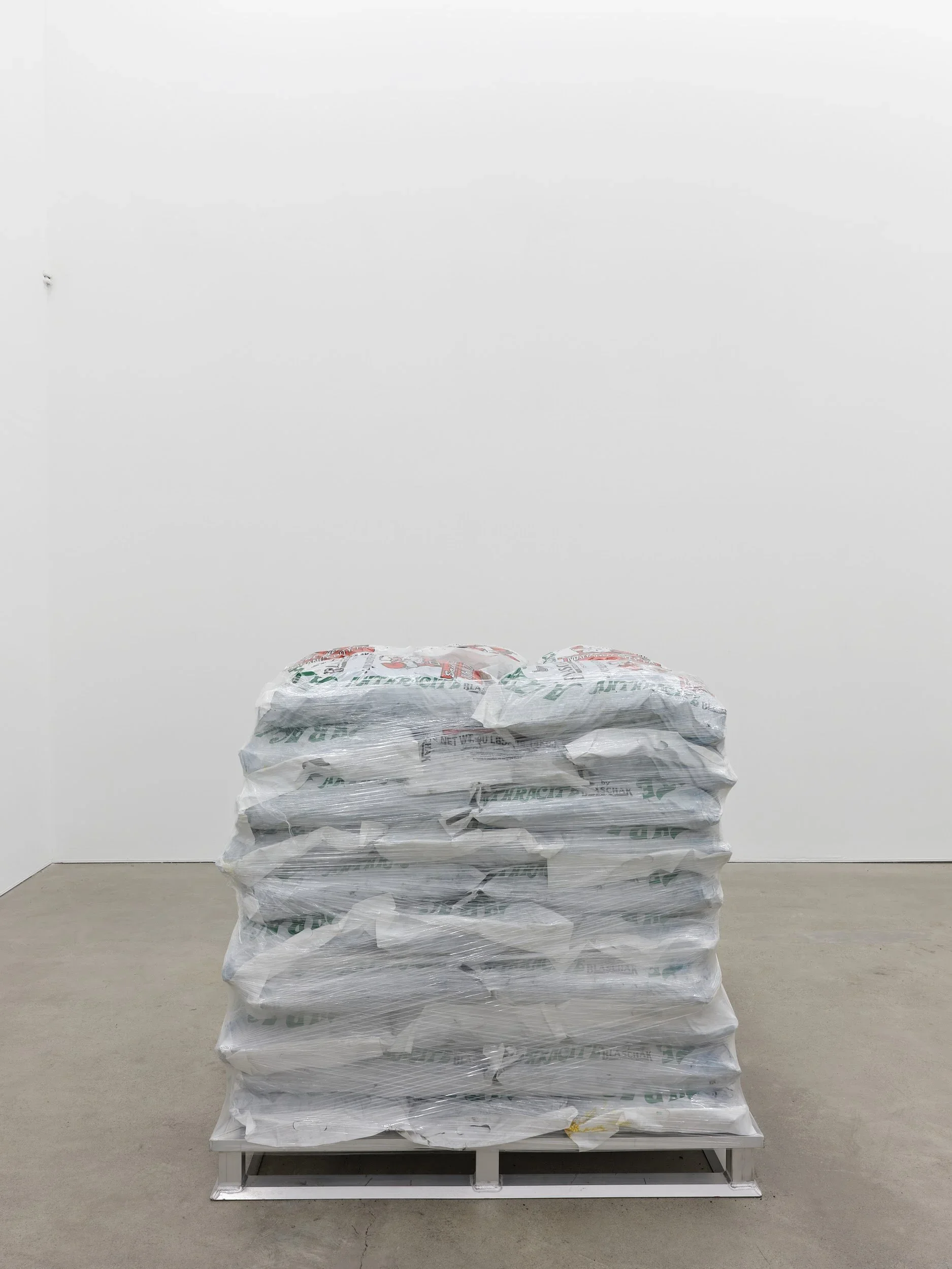 Anthony Discenza. Familiars (S-A-N-T-A), 2024. Bagged anthracite, aluminum pallet, plastic pallet wrap. Courtesy of the artist.