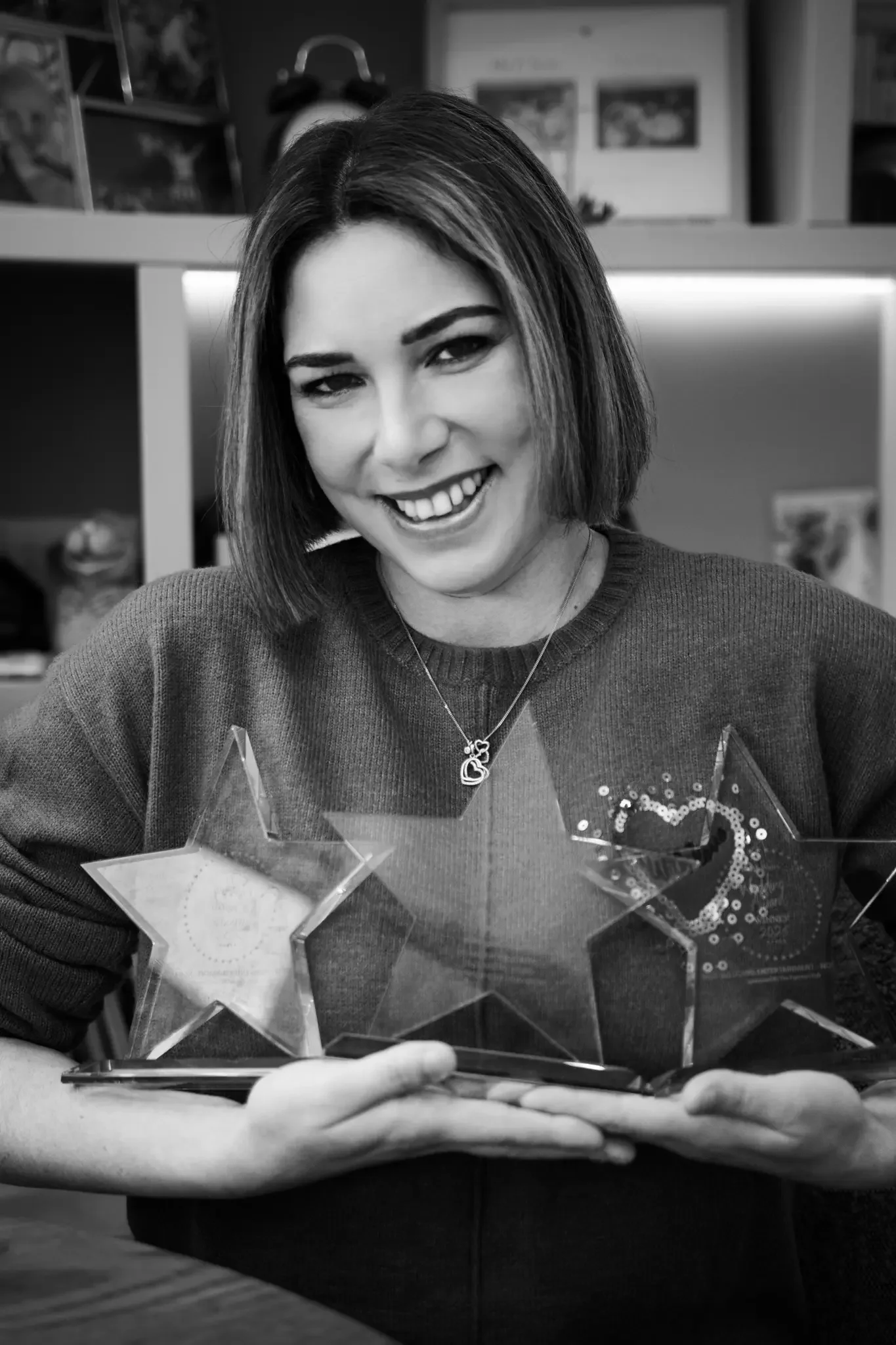 A woman smiling and holding several star-shaped trophies or awards.