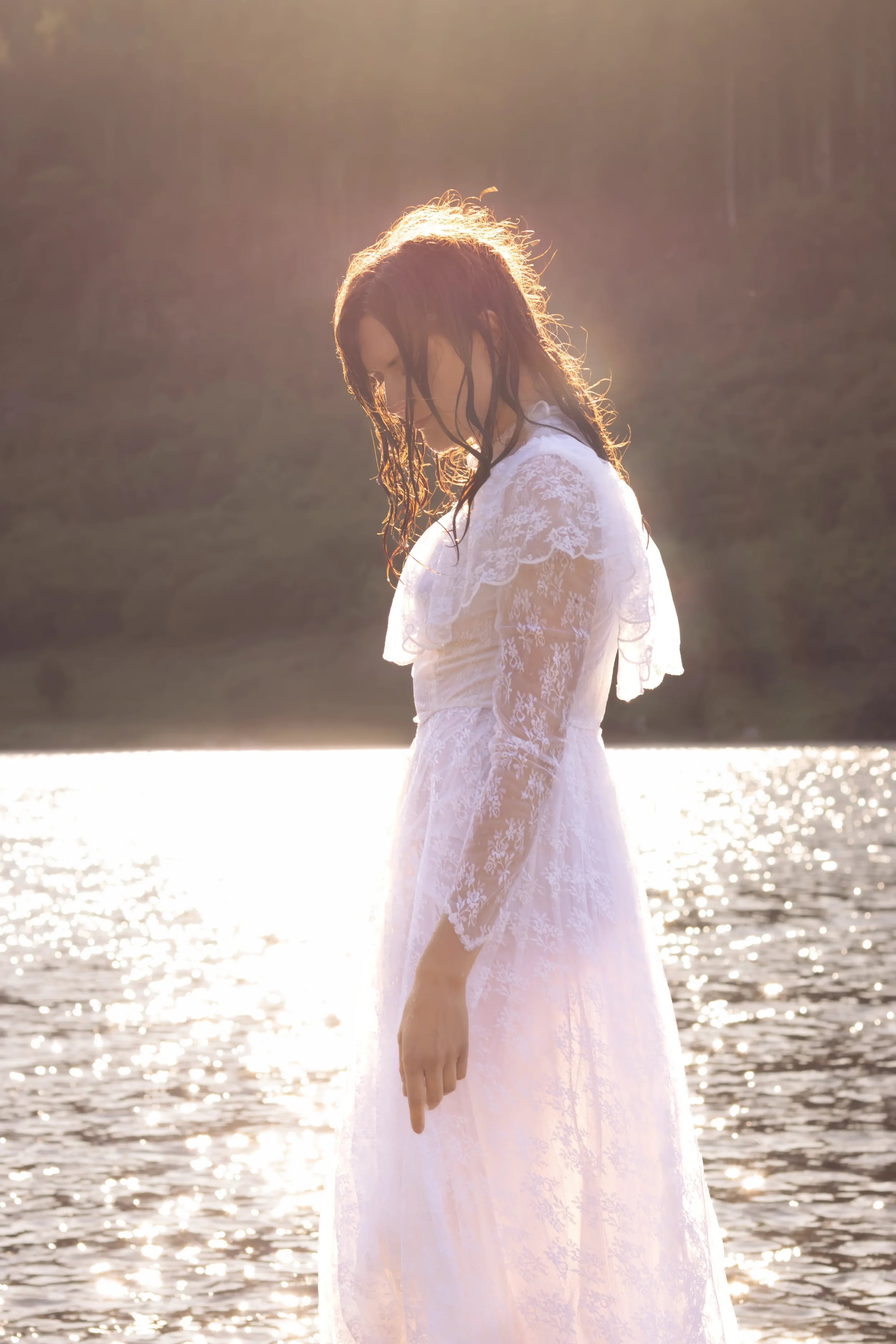 north wales portrait photographer lady standing in a lake in a wedding dress backlit by the setting sun.webp