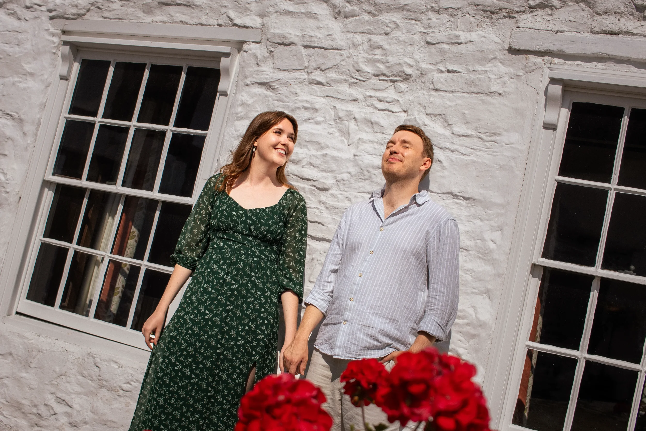 couple-smile-at-each-other-while-leaing-agains-sun-drenched-whhite-wall-of-nantclwyd-y-dre-ruthin-north-wales