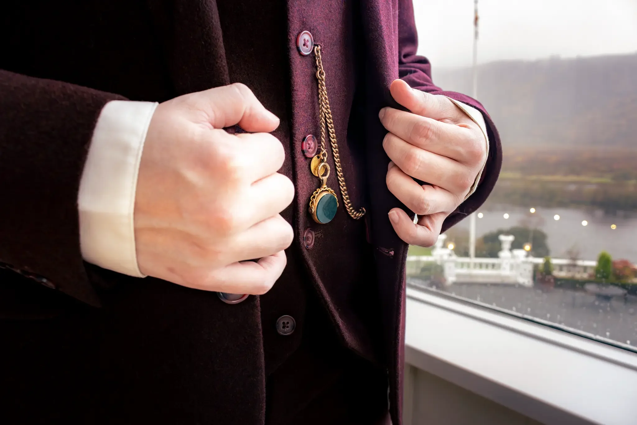 north wales wedding photographer close up shot of bride holding the lapels of her burgundy tweed suit and showing her something old and borrwed pocket watch chain with precious stones.webp