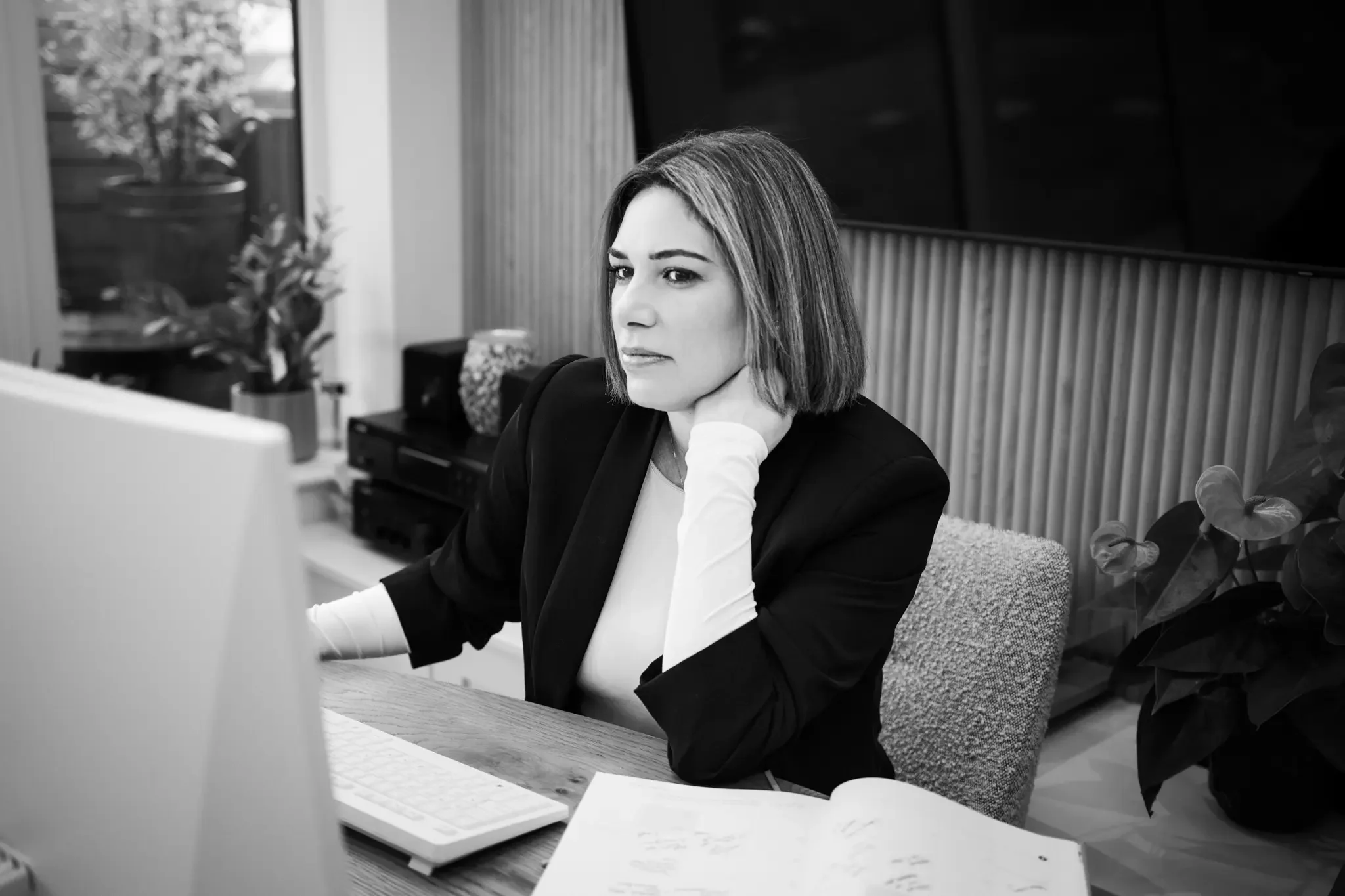 A woman working at a desk in an office, looking at a computer screen with a serious expression.