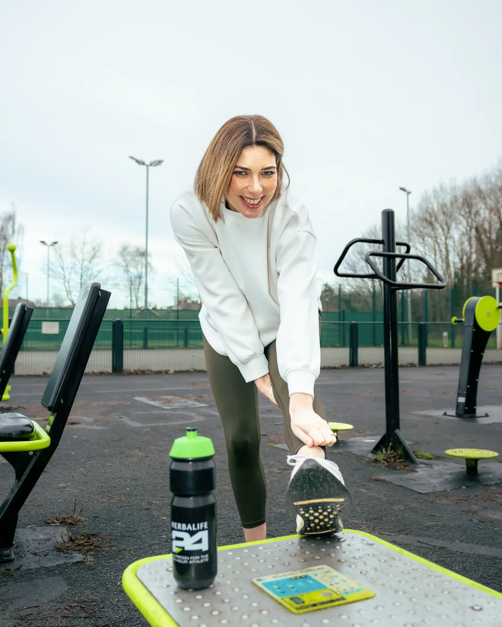 A woman at an outdoor gym stretching her leg.