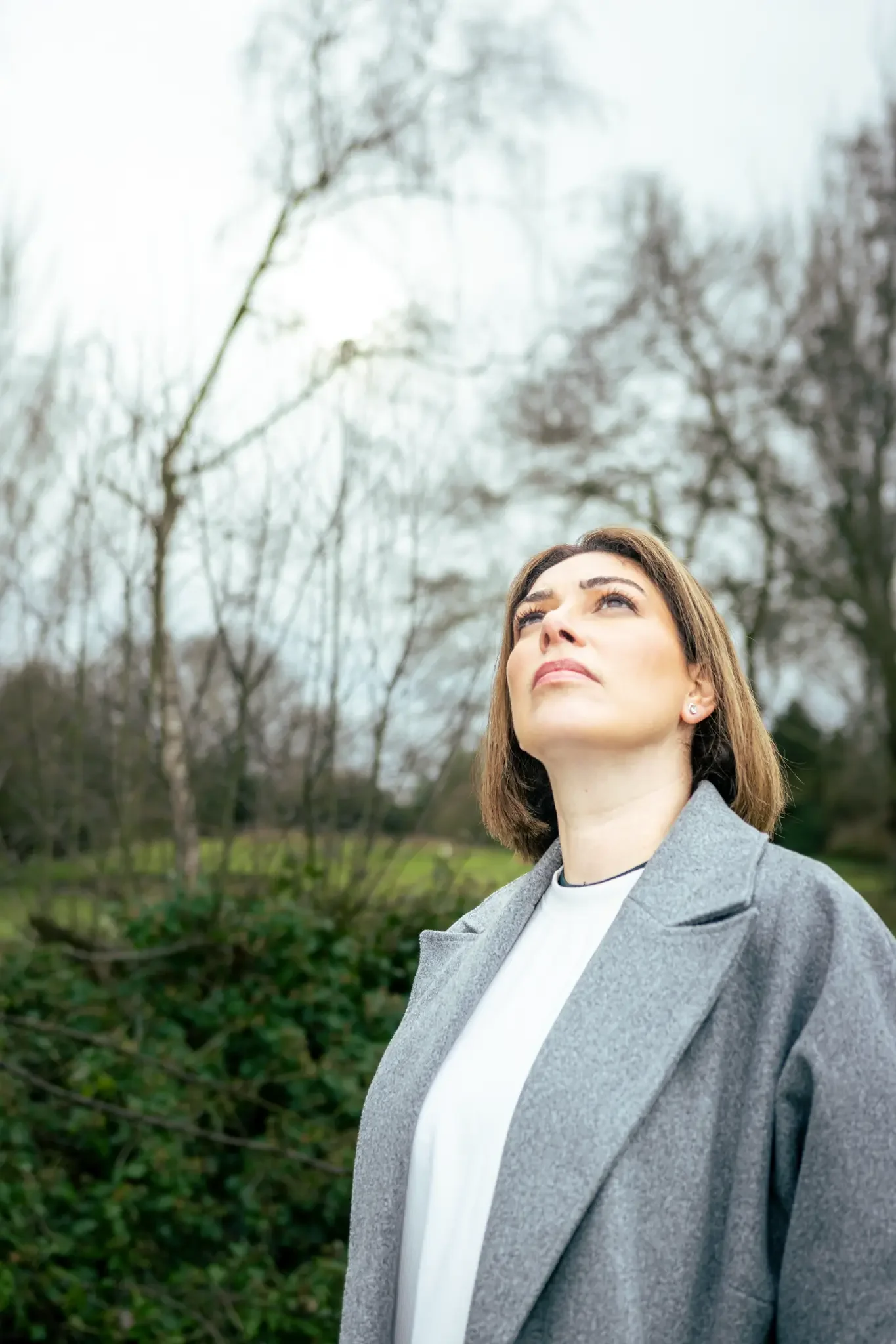 Woman outdoors with trees in the background, looking up with a serious expression.