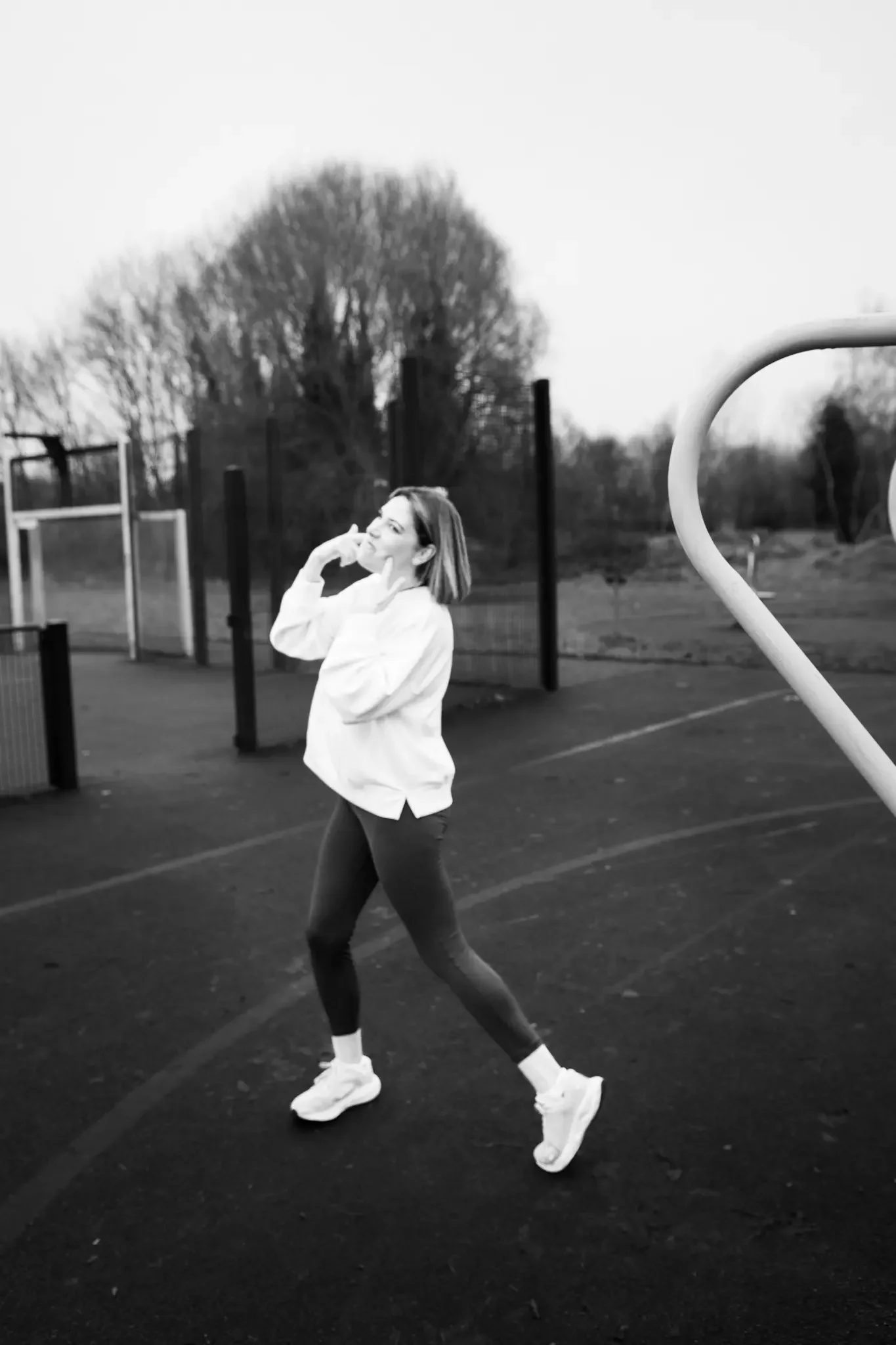 A woman standing on a track, smiling and touching her face, dressed in athletic clothing, with trees in the background.